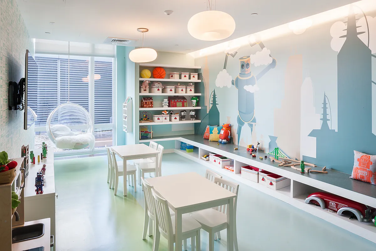 A vibrant playroom featuring a colorful mural on the wall and assorted bright furniture for children.