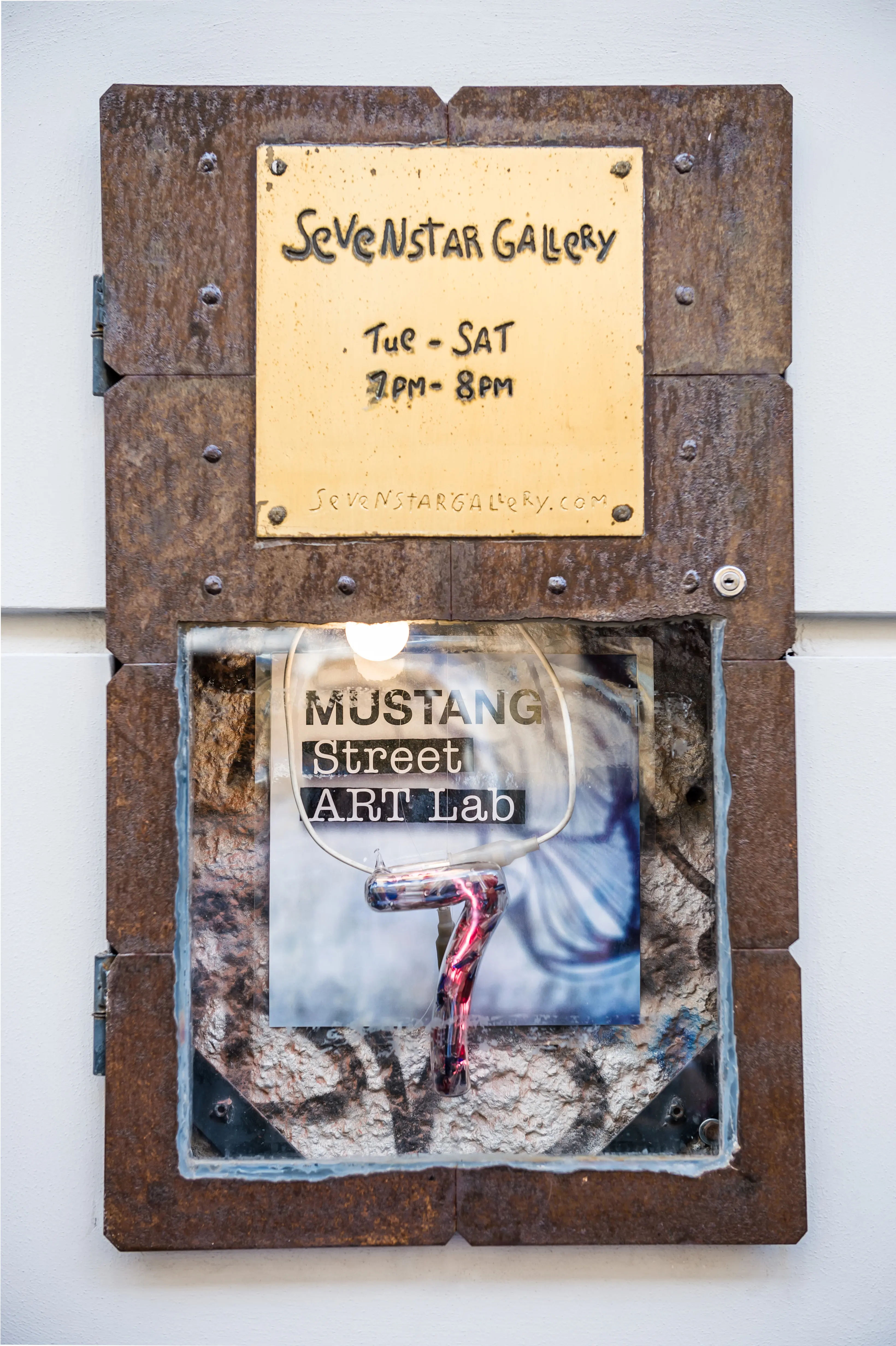 Rusty metal sign of the Sevenstar Gallery with a MUSTANG Street ART Lab poster behind glass and an engraved glass plate.