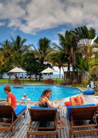 Guests relax by the pool and kids play at Uprising Beach Resort in Pacific Harbour Fiji surrounded by palm trees