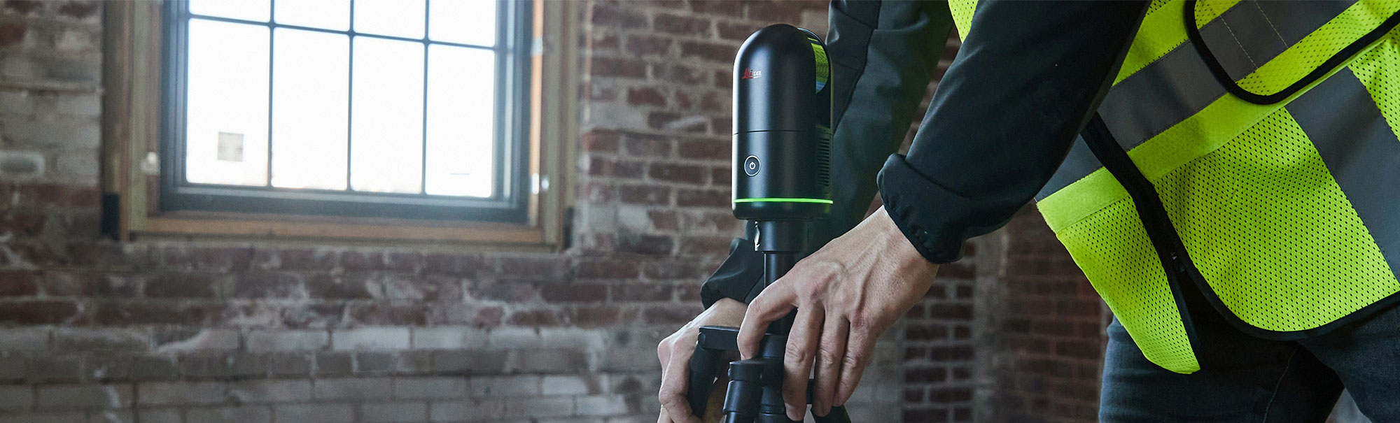 Architect in a hi-vis vest operating a Leica BLK360 3D laser scanner on a tripod inside a brick building.