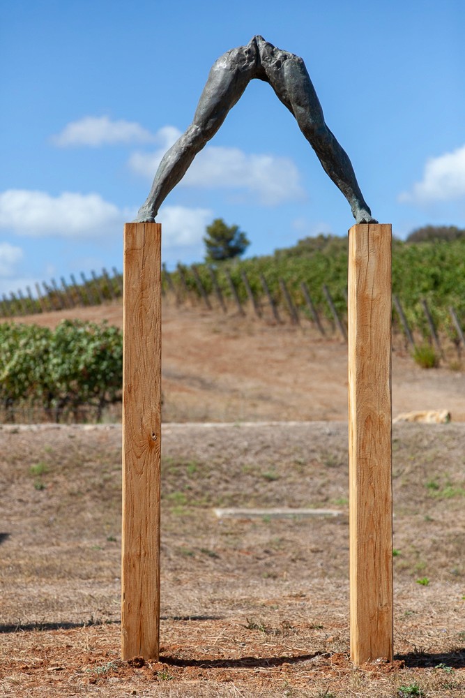 Arch-shaped structure made of wood, set against a blue sky and grassy landscape.