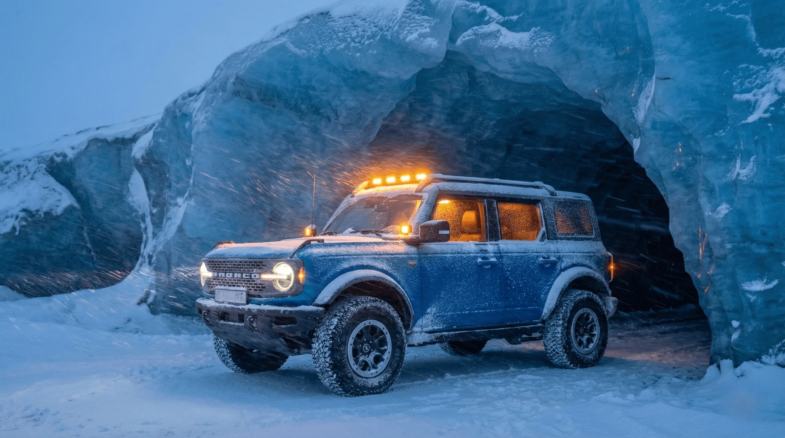 Blue Ford Bronco with roof lights on parked inside a stunning blue ice cave.