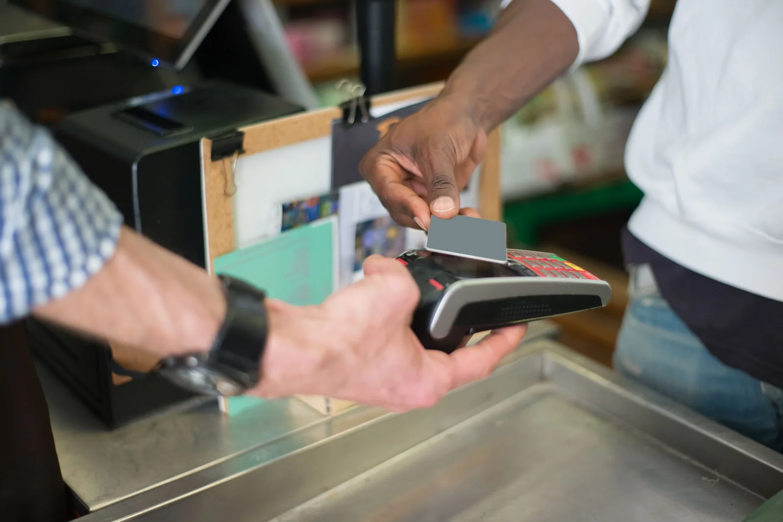A shopper taps a card on a payment terminal at a checkout counter.