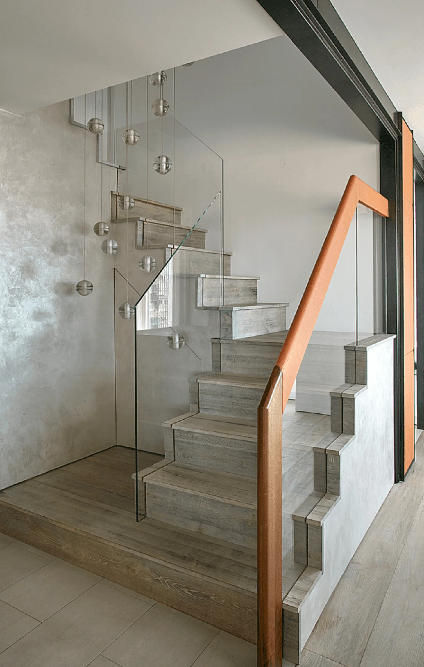 A staircase with glass balustrade and a copper-toned handrail, lit by a cluster of hanging glass globe pendants