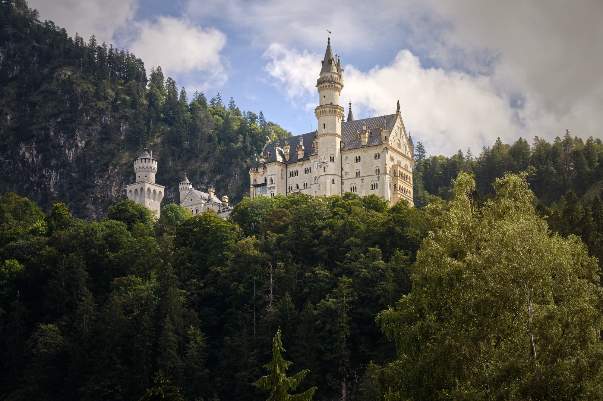 Schloss Neuschwanstein mit dramatischem Himmel und umgebendem Bergwald im Allgäu.