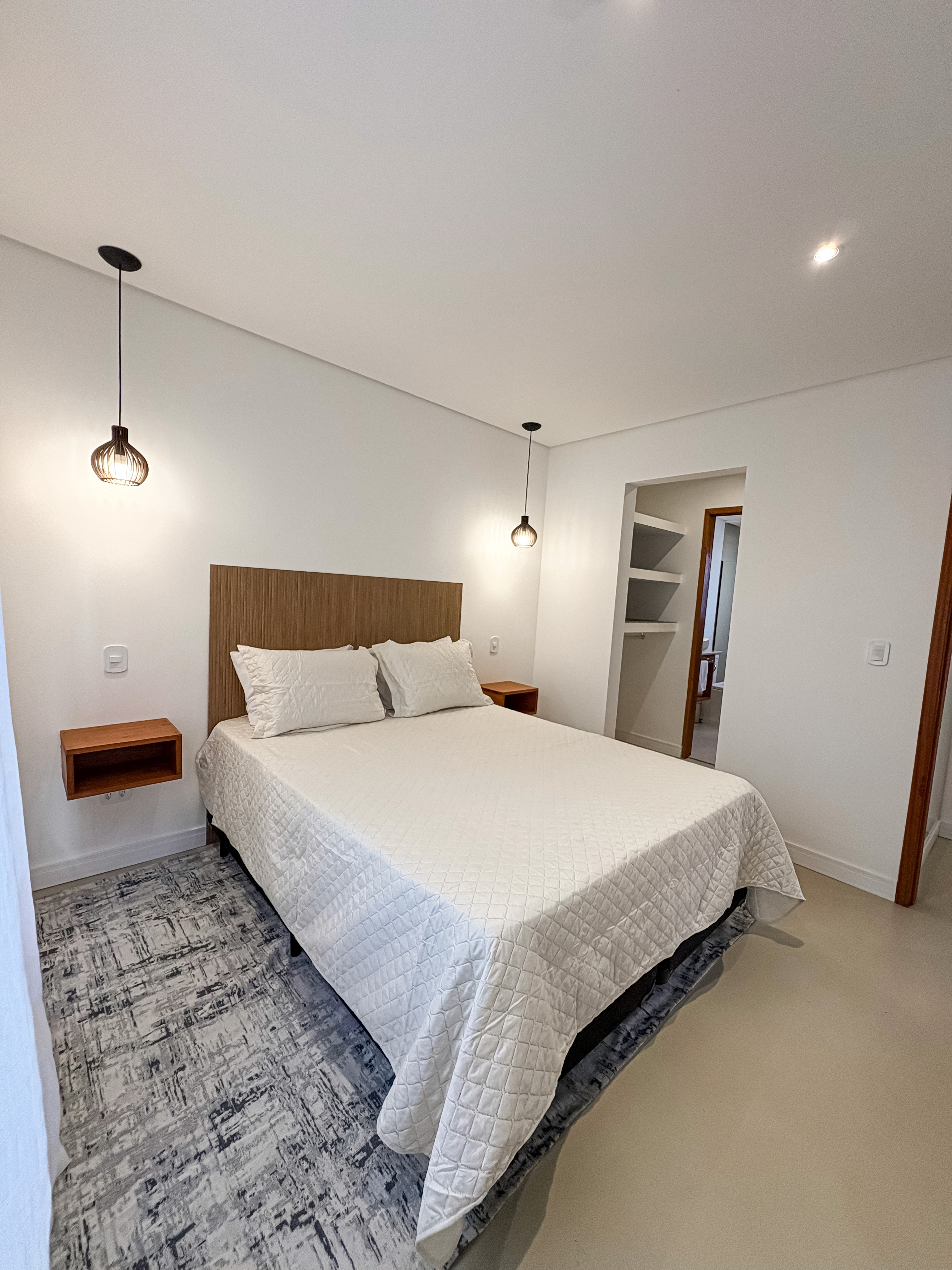 spacious open-plan suite with king bed, sofa lounge, light wood flooring, and ocean views through sliding glass doors.