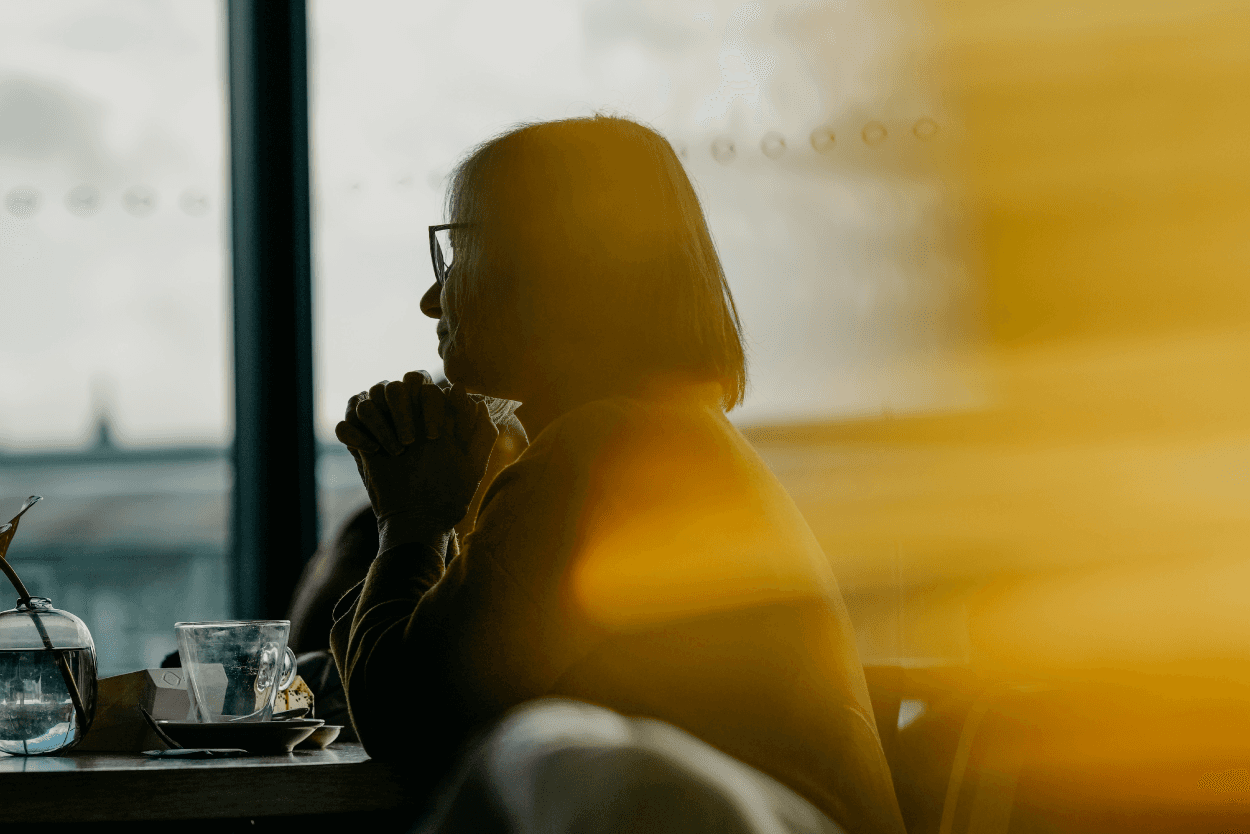 Woman sits at a coffee table, looking out of the window.