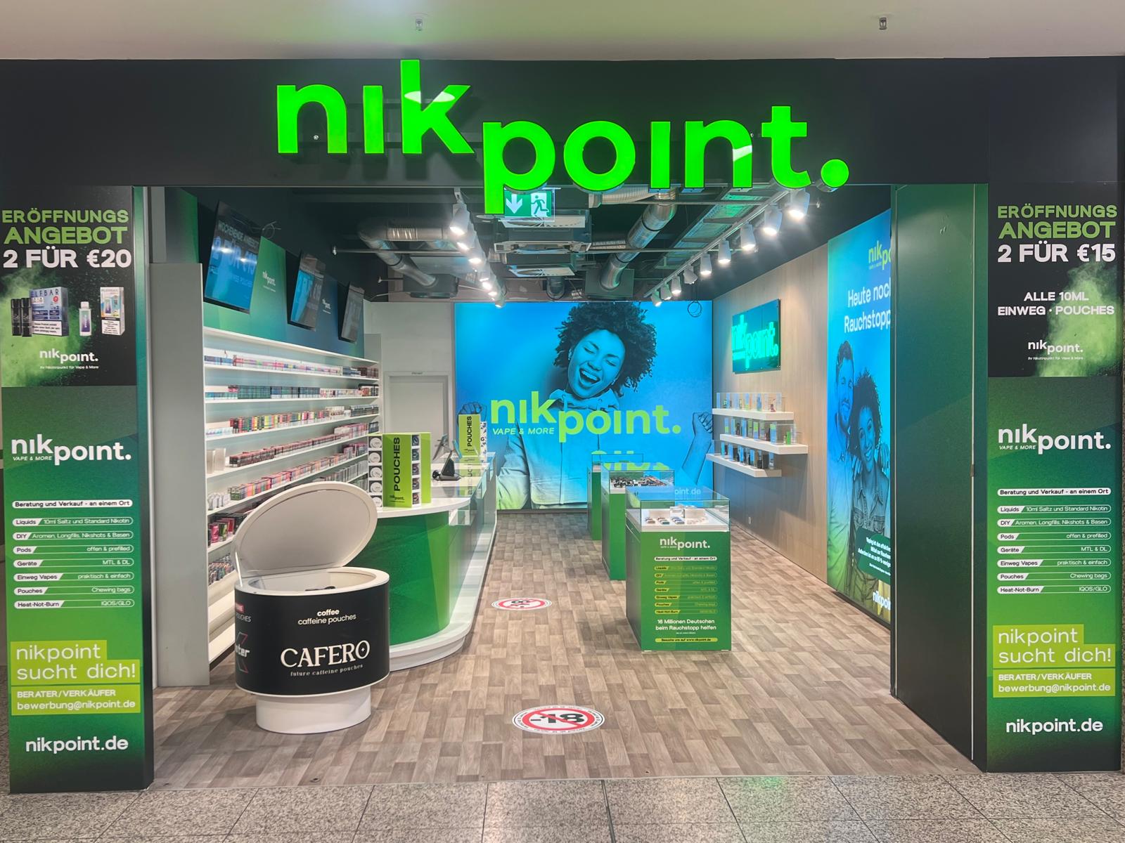 Nikpoint E-Zigaretten-Store in Leverkusen mit moderner Glasfront, grünem Leuchtschild und hell beleuchtetem Innenraum mit weißen Regalen und Markenfarben in Grün.