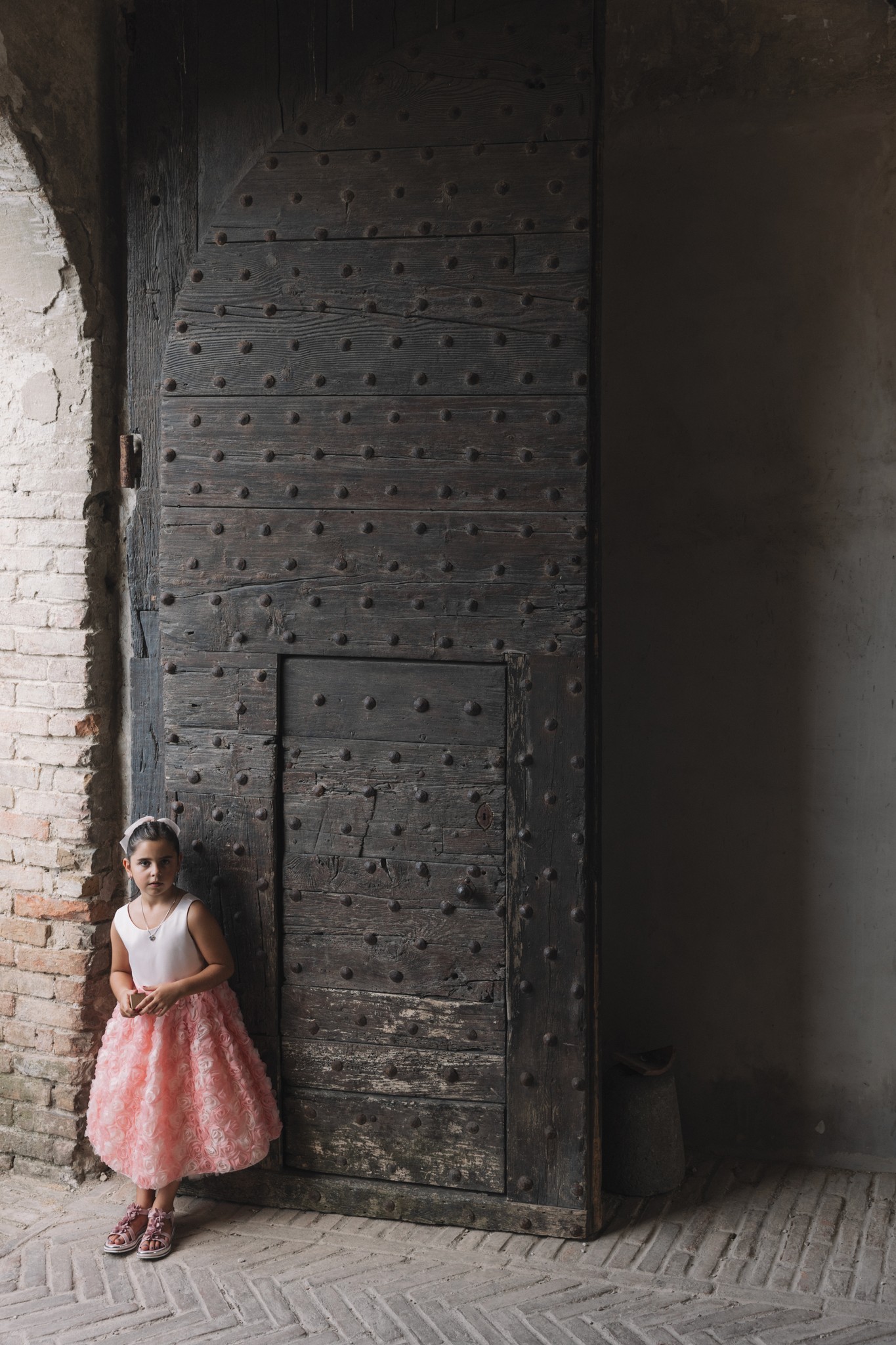 Sposa in gonna rosa appoggiata a una porta in ferro battuto medievale nel Parco di Montebello, ritratto di matrimonio