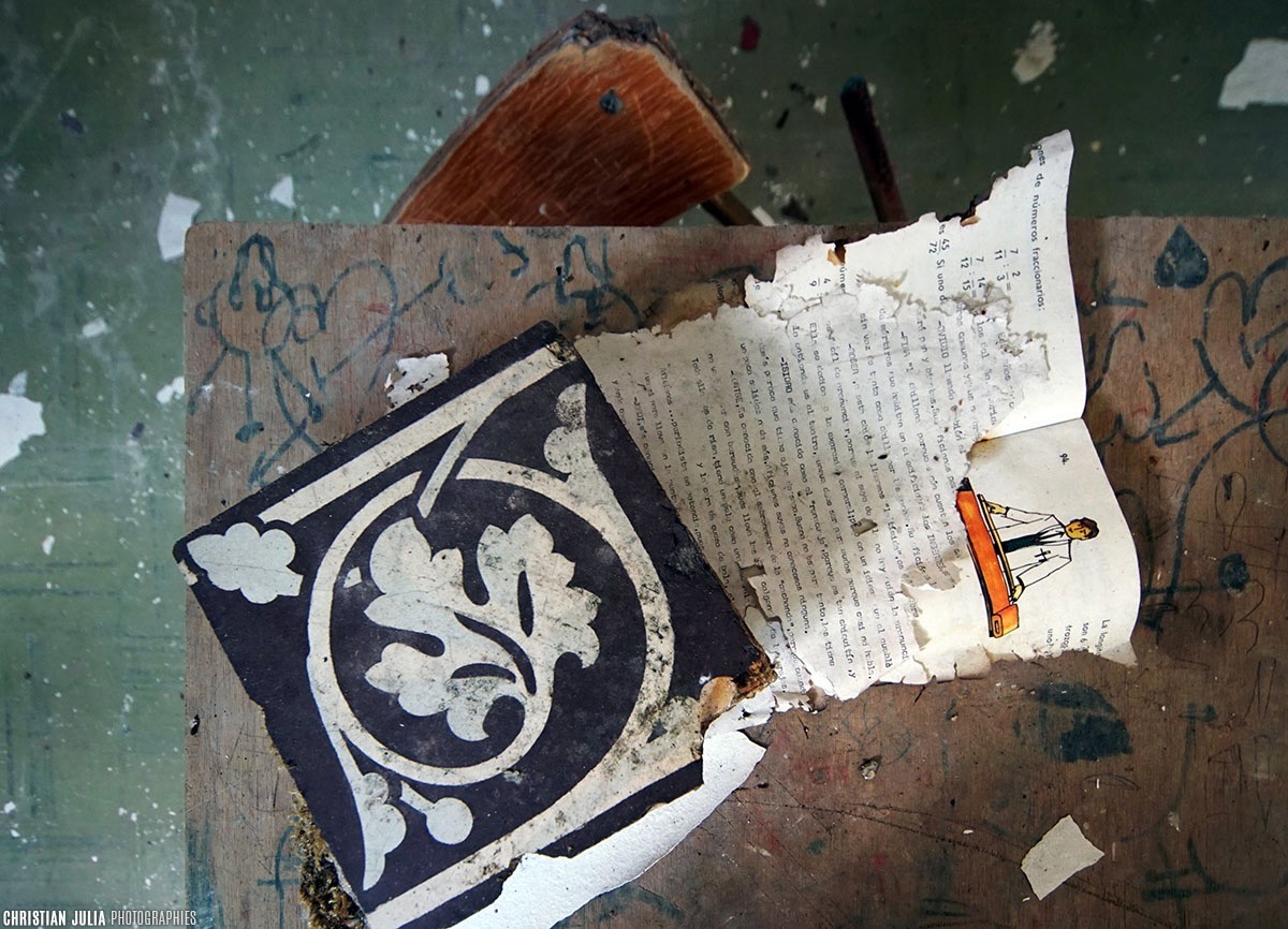 A torn printed page and a patterned floor tile lie on a battered surface.