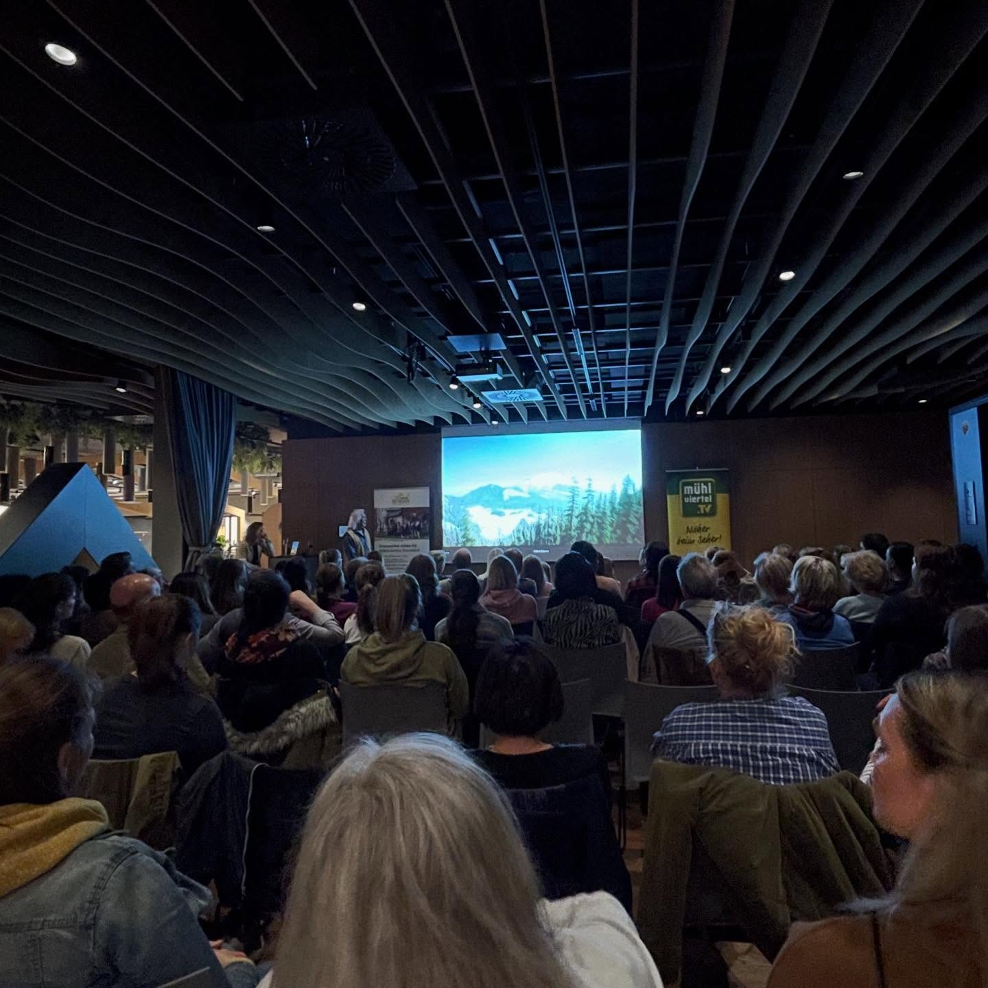 Leute sitzen vor einer Leinwand, vorne spricht Erich Pröll.