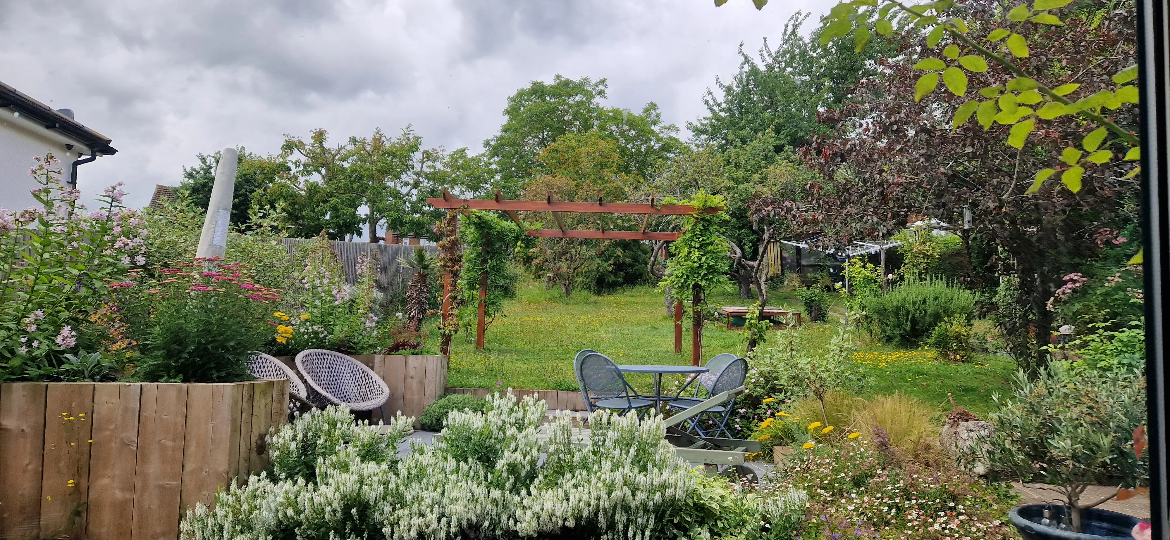 A lush garden with various plants, trees, and a cloudy sky in the background, showcasing a serene outdoor space.