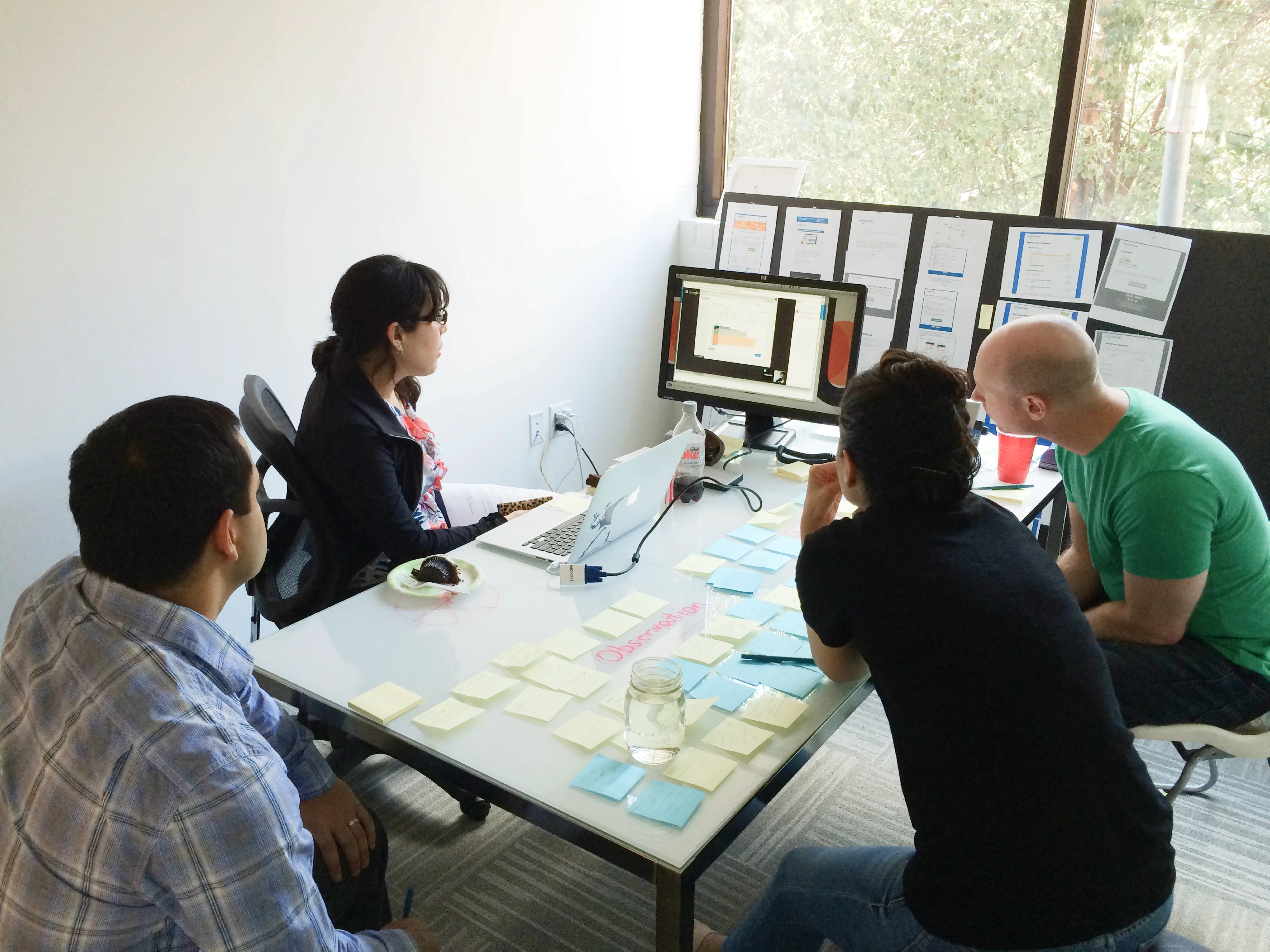 Me plus team members sitting around a table in an office, watching a remote user research session and surrounded by sticky notes.