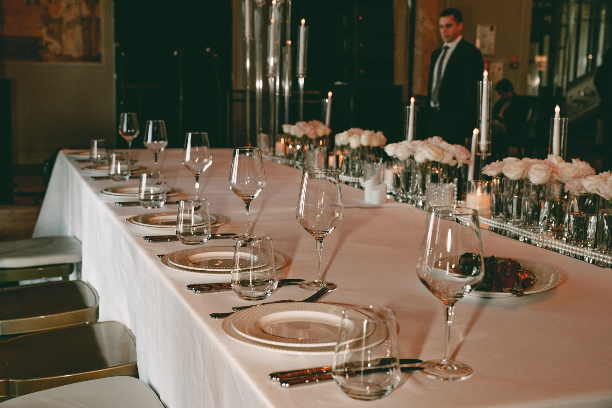 საქორწილო საპატიო მაგიდა დიდი ფანჯრების წინ, სანთლების კომპოზიციით, ვარდისფერი ყვავილებით და კლასიკური დეკორით