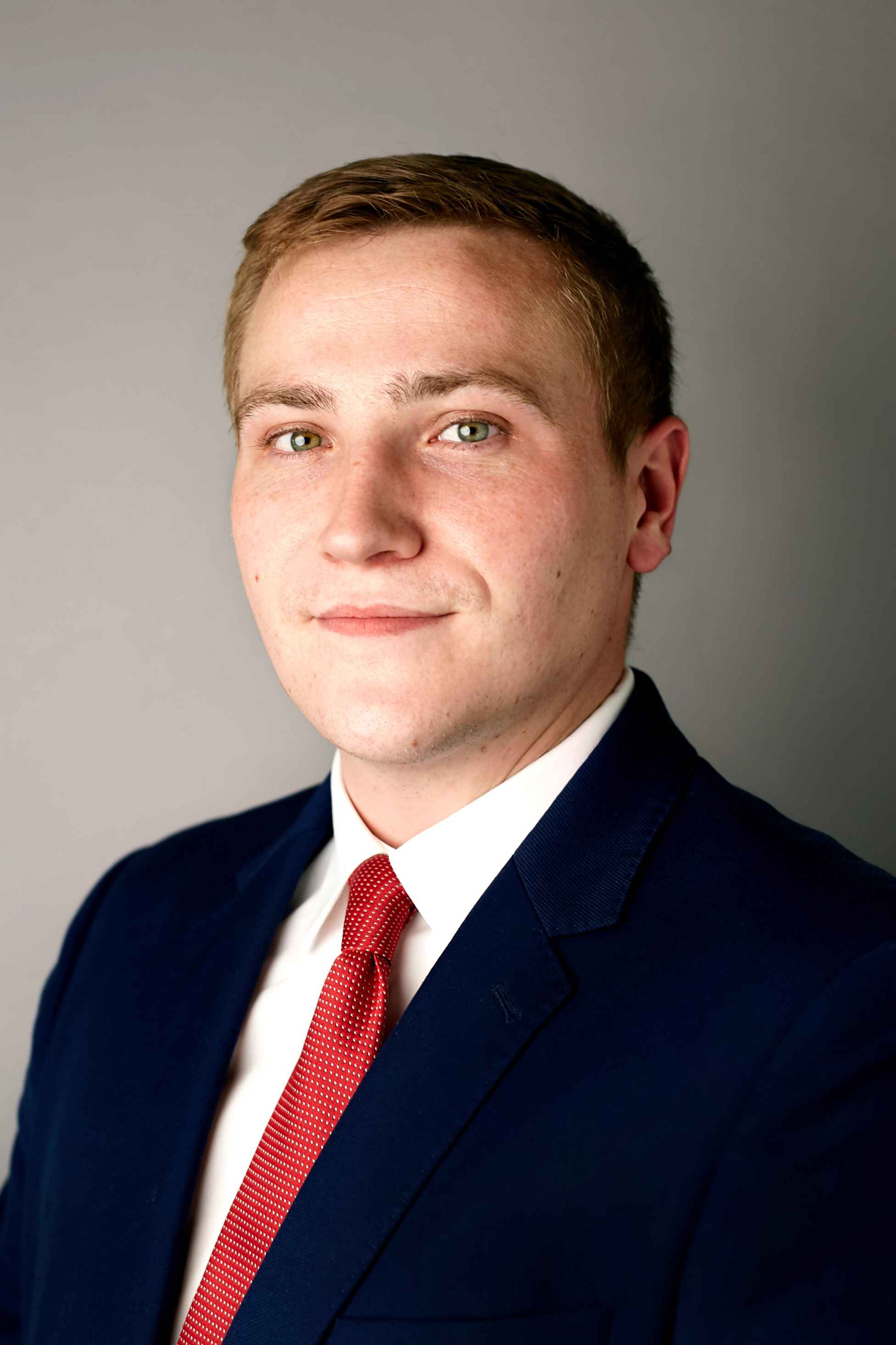 Man in navy suit and red tie looking at camera.