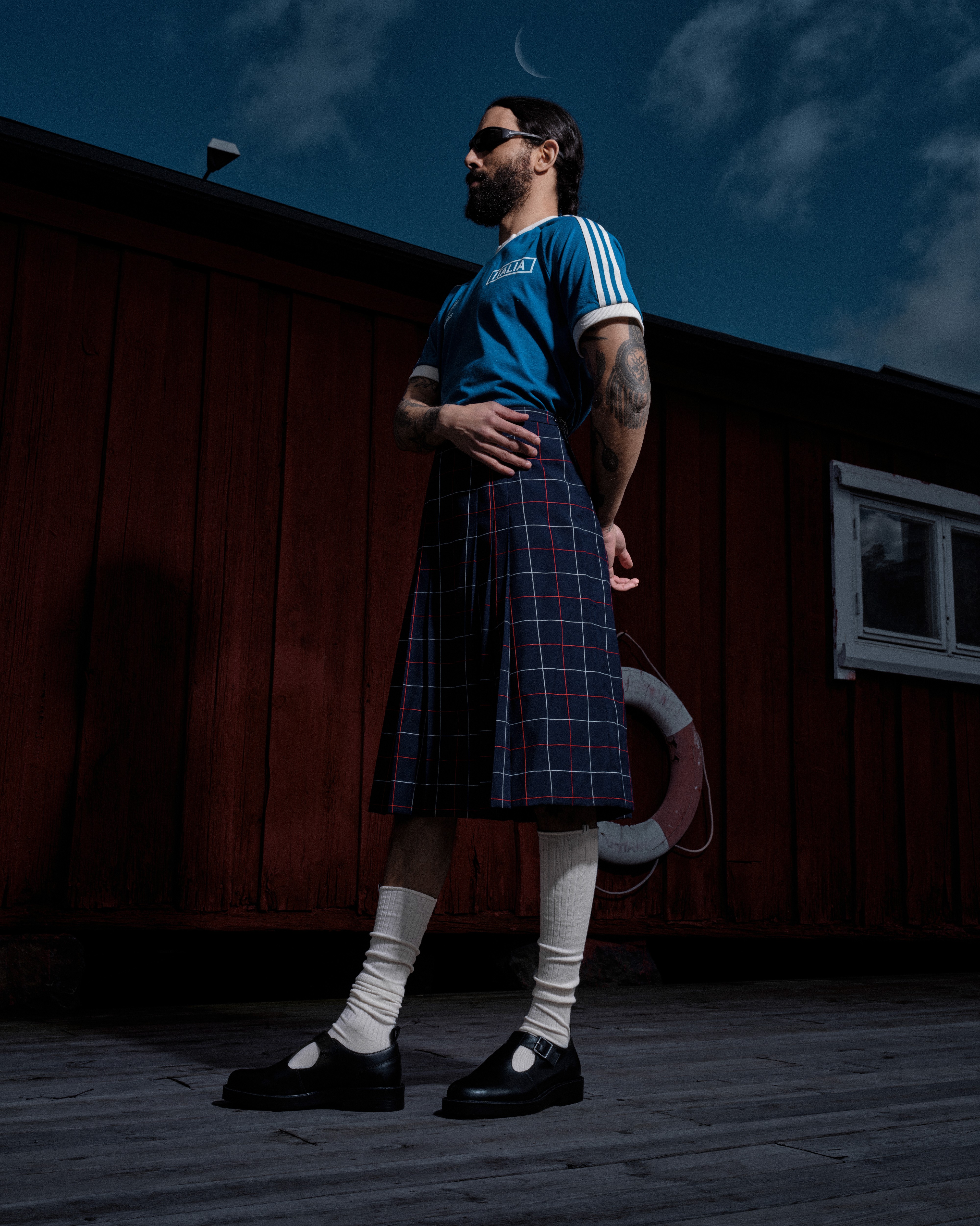 Un homme porte un kilt, un maillot de foot et des chaussettes blanches montantes