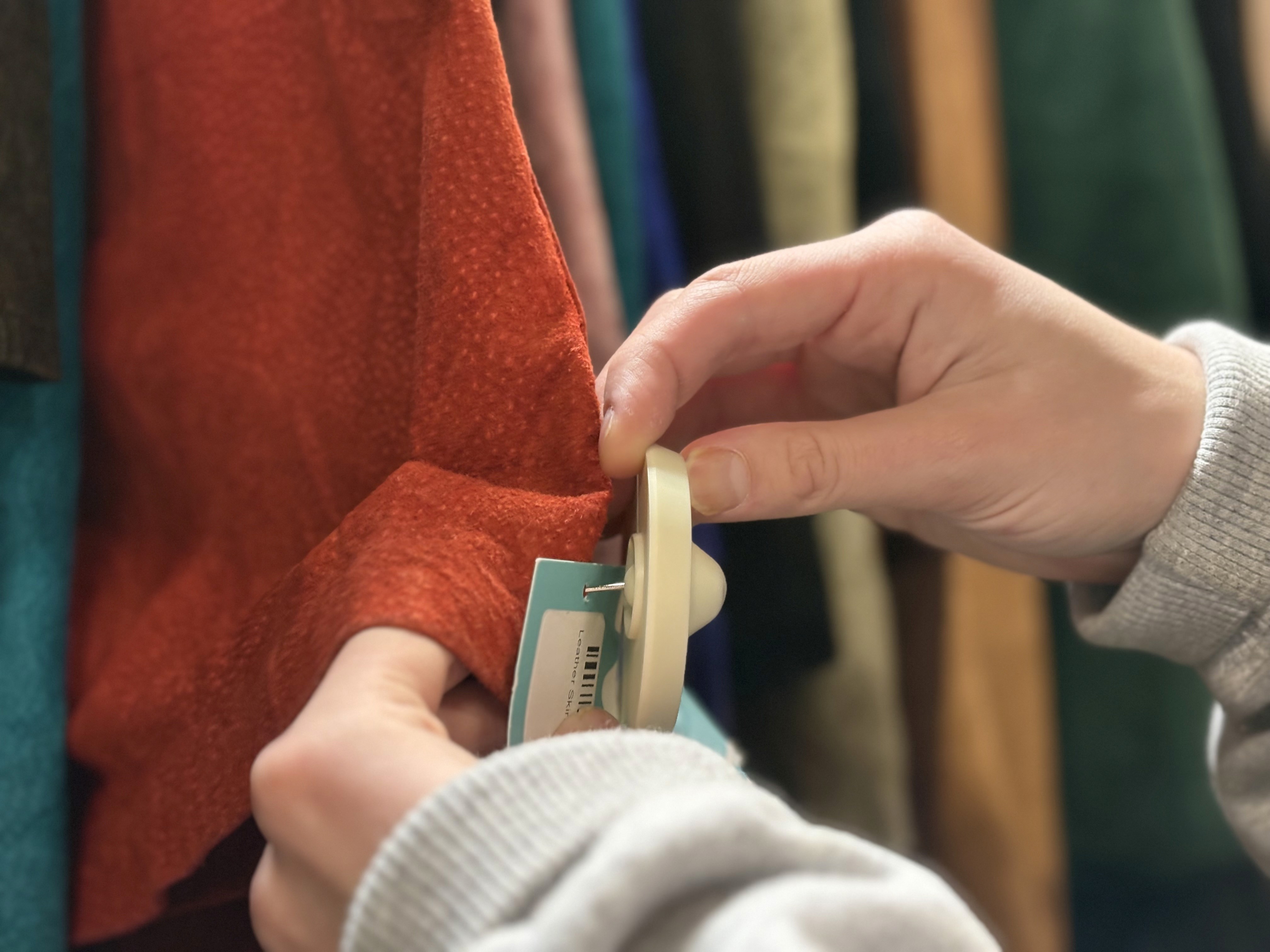 Person removing security tag from red leather skirt on clothing rack.