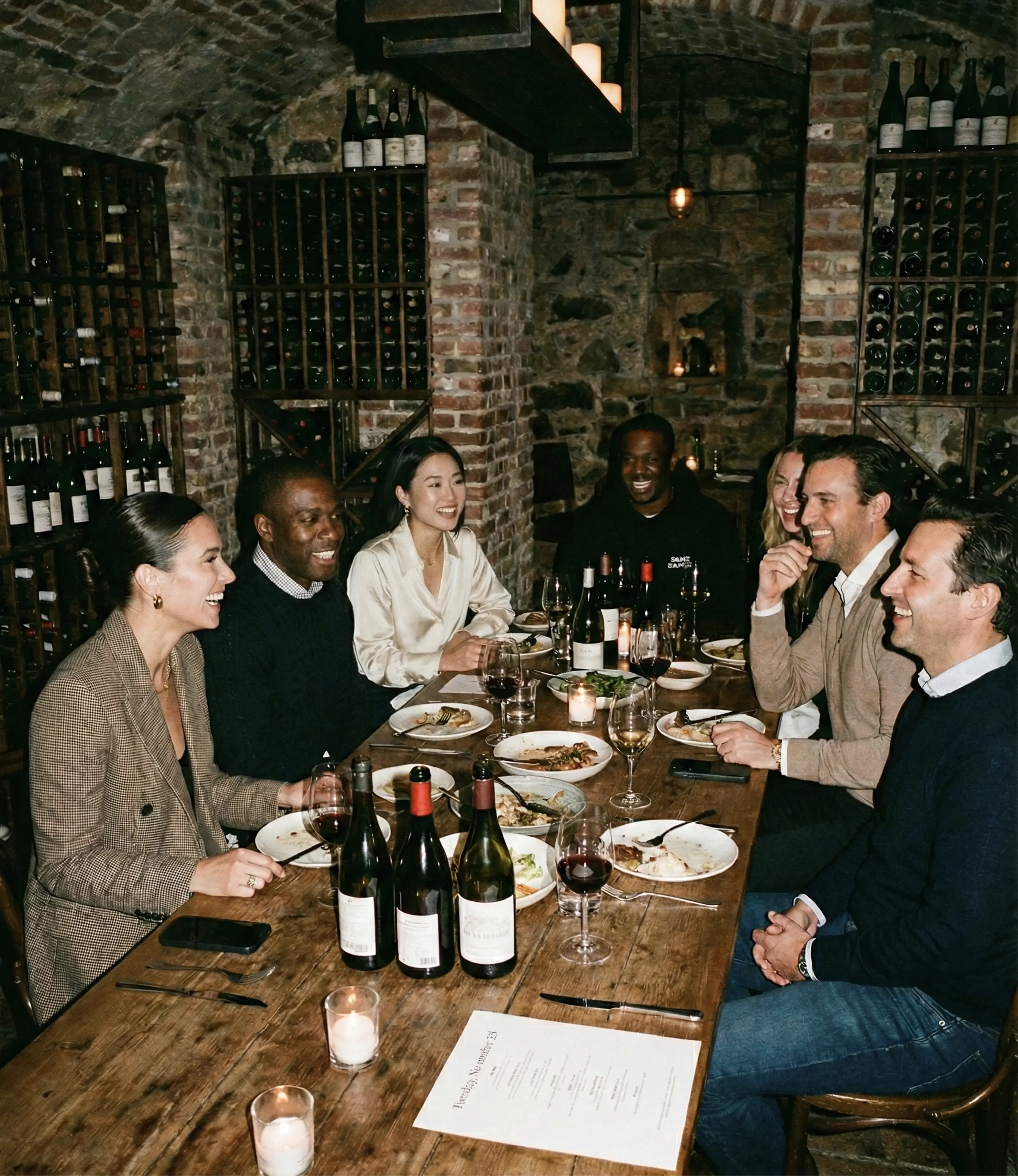 White plate with roasted carrots served on green sauce, topped with almonds and fresh herbs, held by a hand over a dark table.