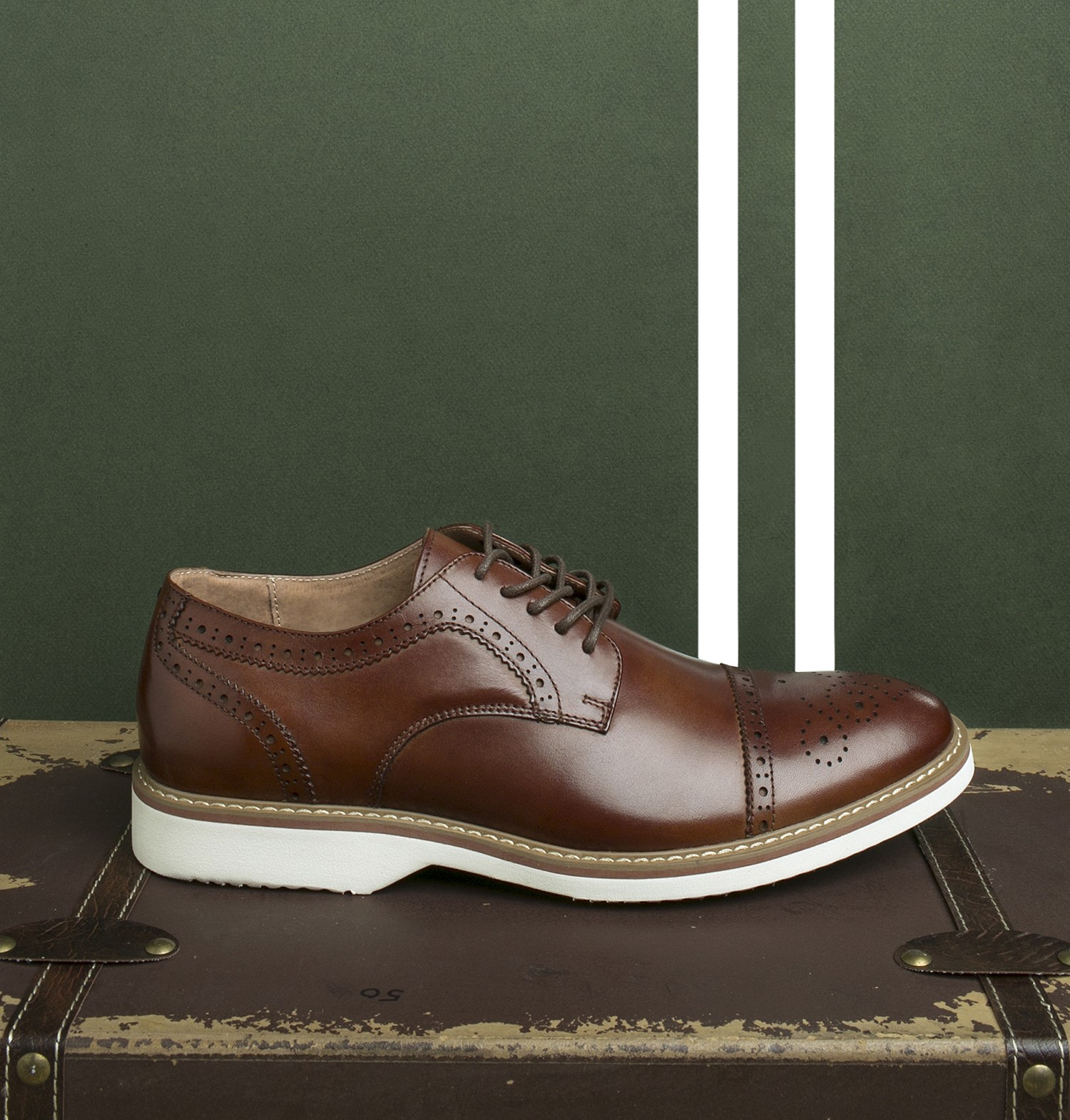 Florsheim brown leather brogue shoe displayed on a vintage suitcase against a green background with white stripes.