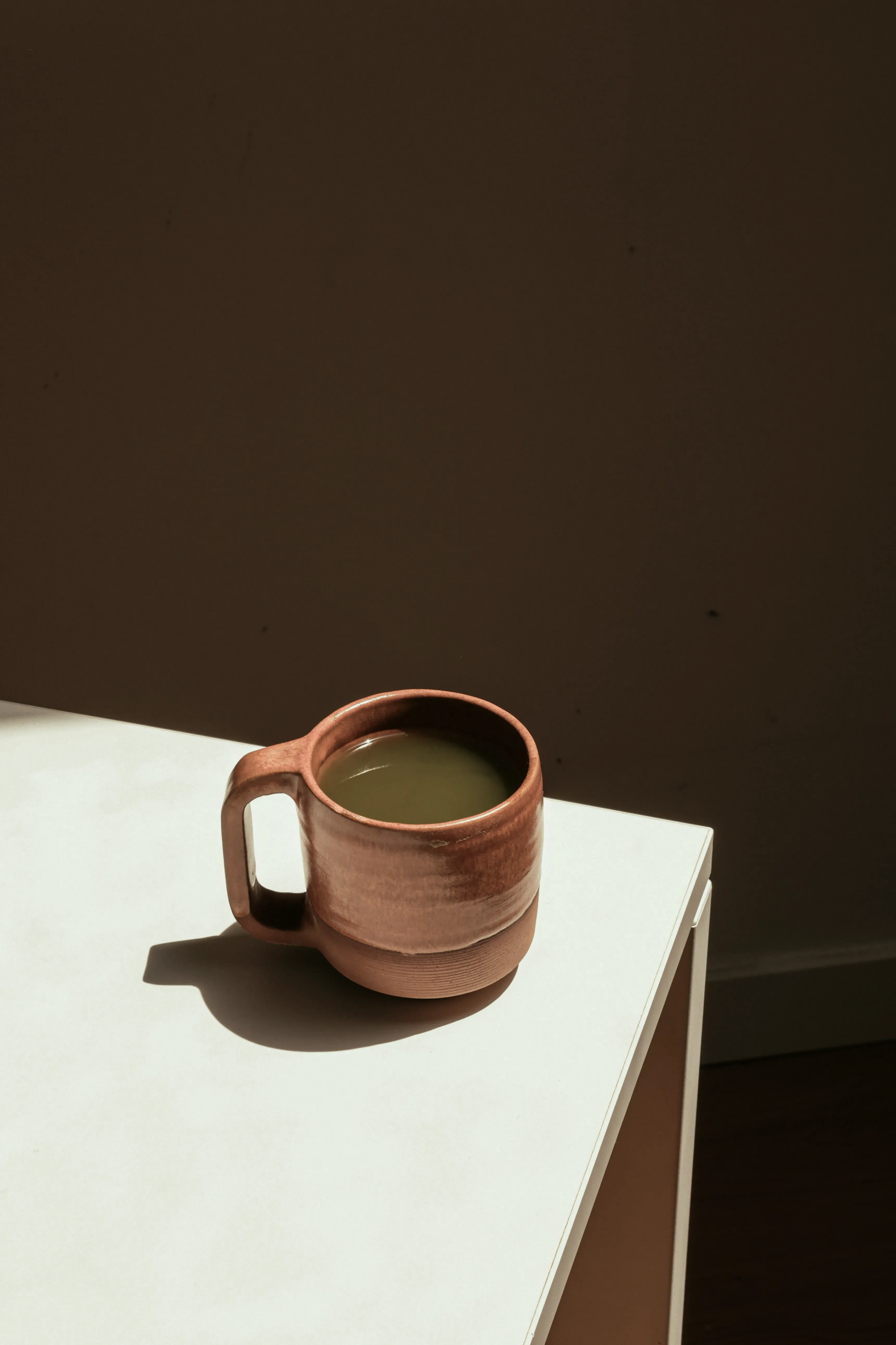 A scene of a brown ceramic mug on the edge of the table