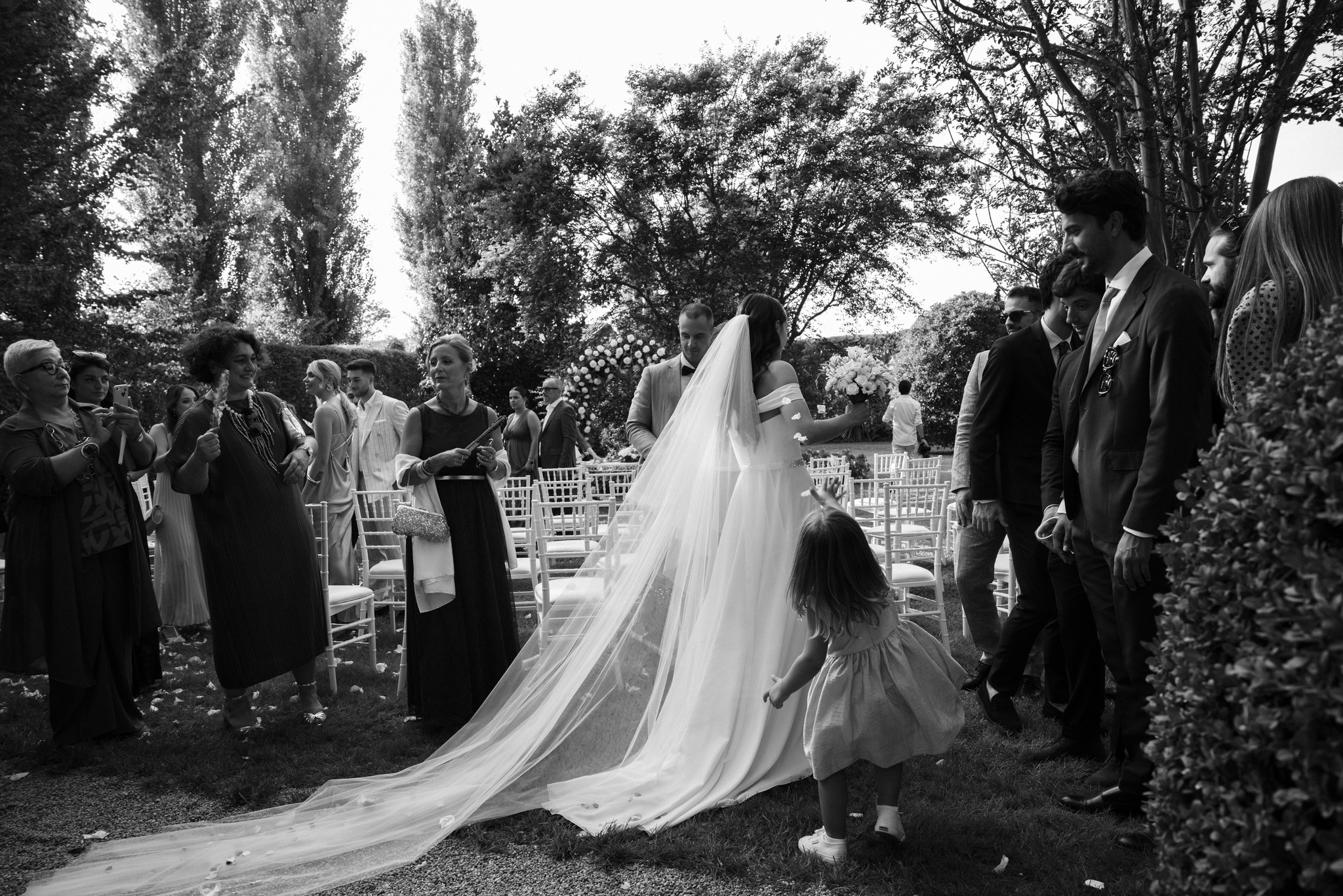 Sposa con velo lungo nel giardino di Villa Negri durante la cerimonia, circondata da ospiti e sedie bianche