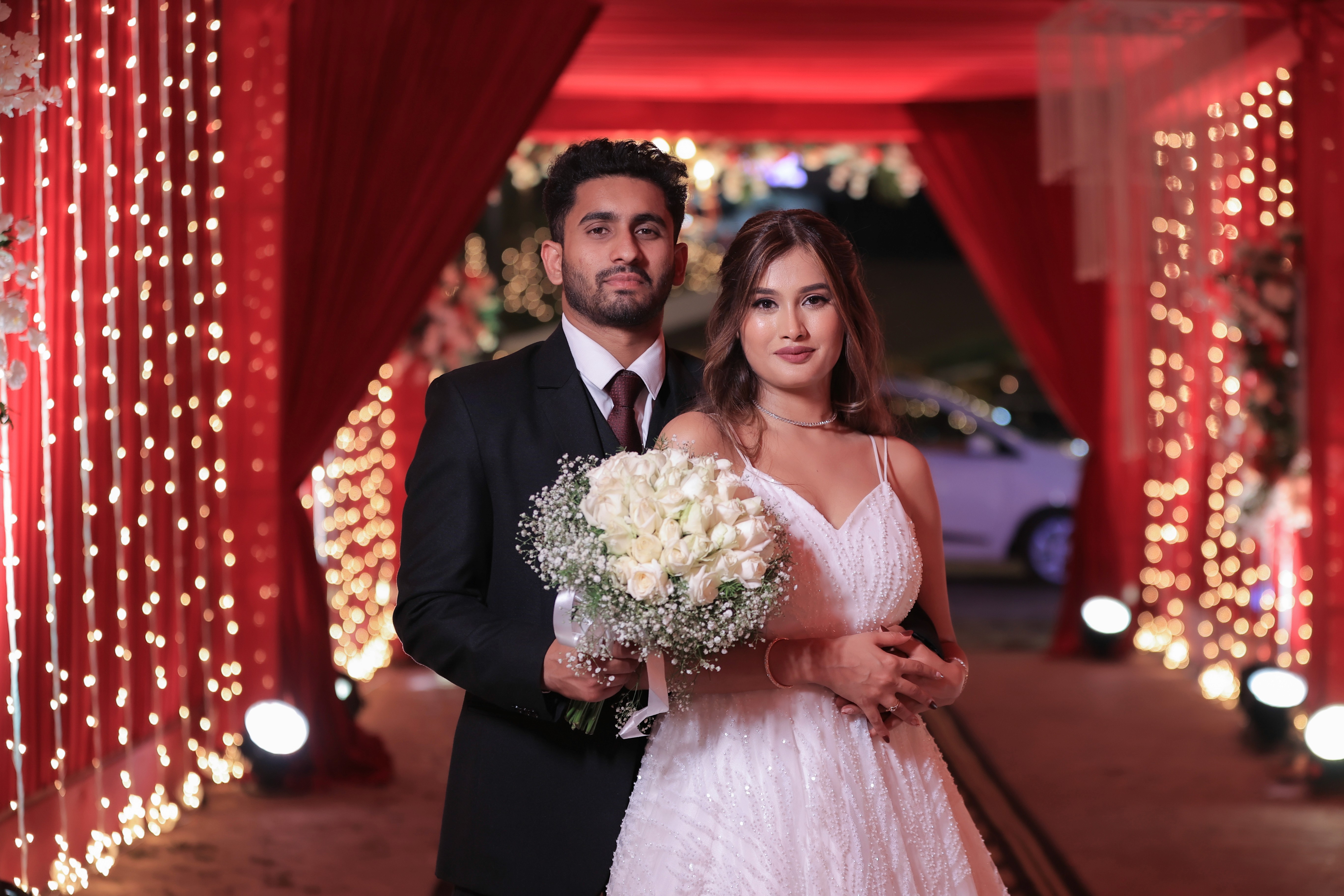 Bride and groom posing together under red drapery at a wedding venue