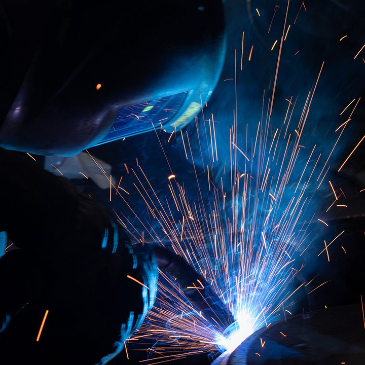 Spawacz w masce spawa metal, iskry i jasne światło. Zbliżenie na proces spawania, praca w warsztacie.