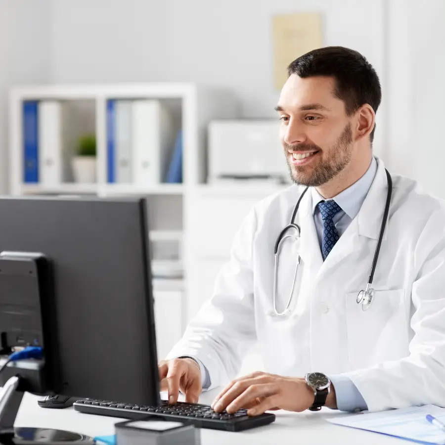 AI scribe for doctors enhances efficiency, as shown by a smiling physician documenting patient notes on a computer in a modern office