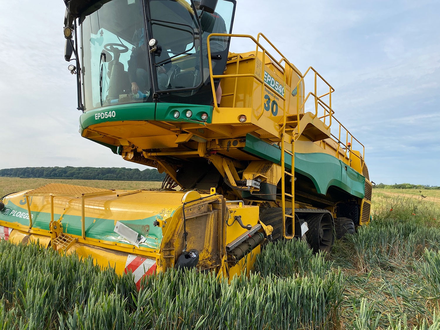 Damage to the front of a Ploeger harvester. The vehicle is bright yellow and green and is in a field