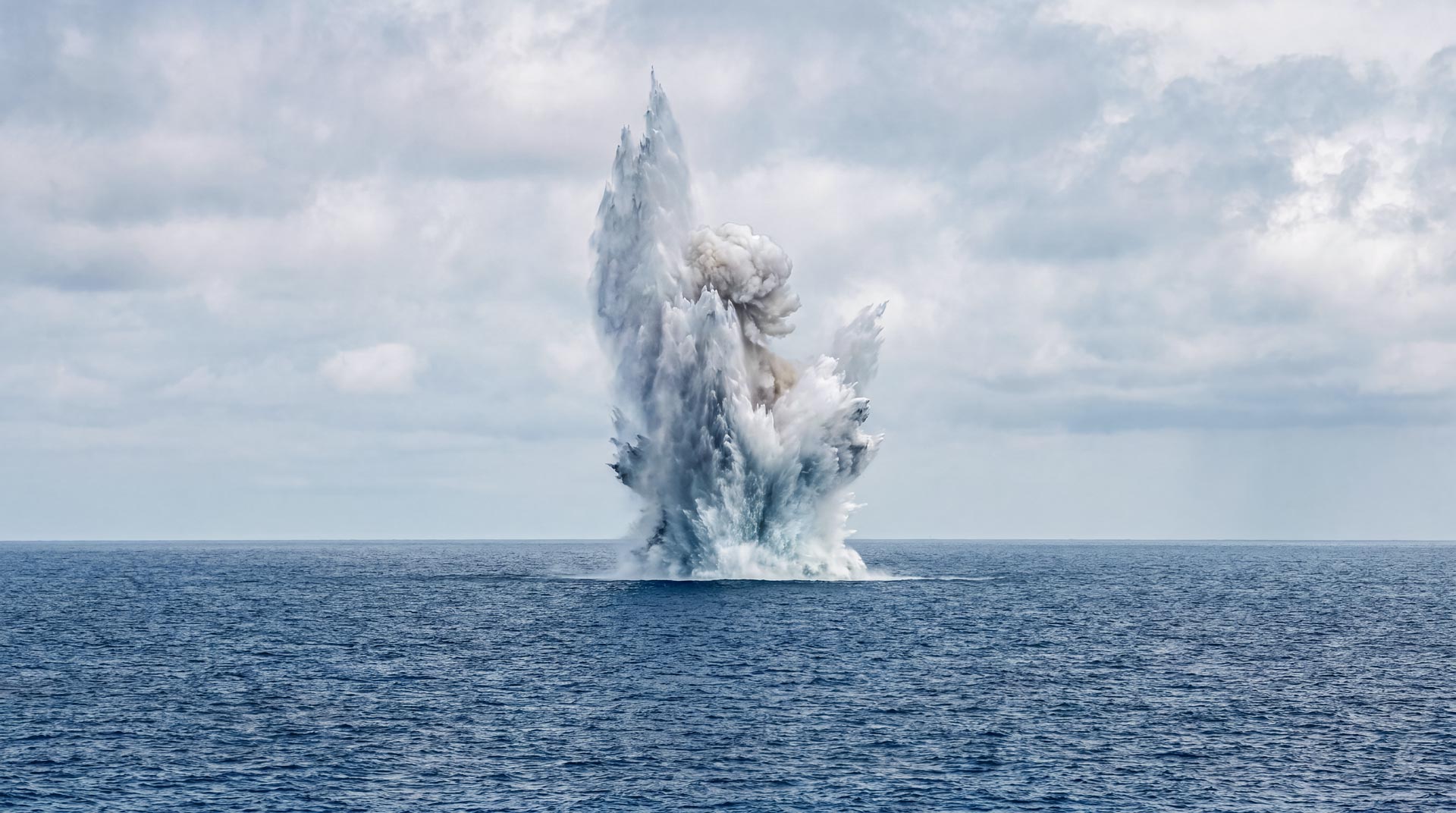 Controlled underwater demolition explosion during EOD operations, destroying a submerged explosive threat at sea.