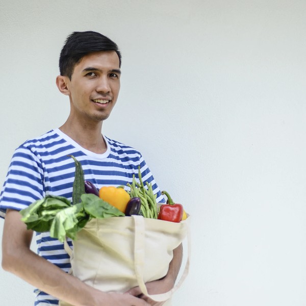 image of man holding reusable tote bag made from recycled material and filled with groceries