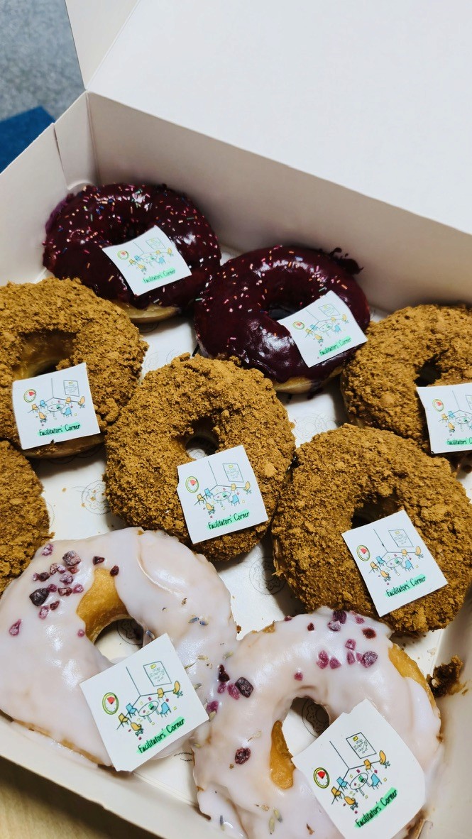 Box of assorted donuts decorated with Facilitators’ Corner logo, served during a workshop or team event