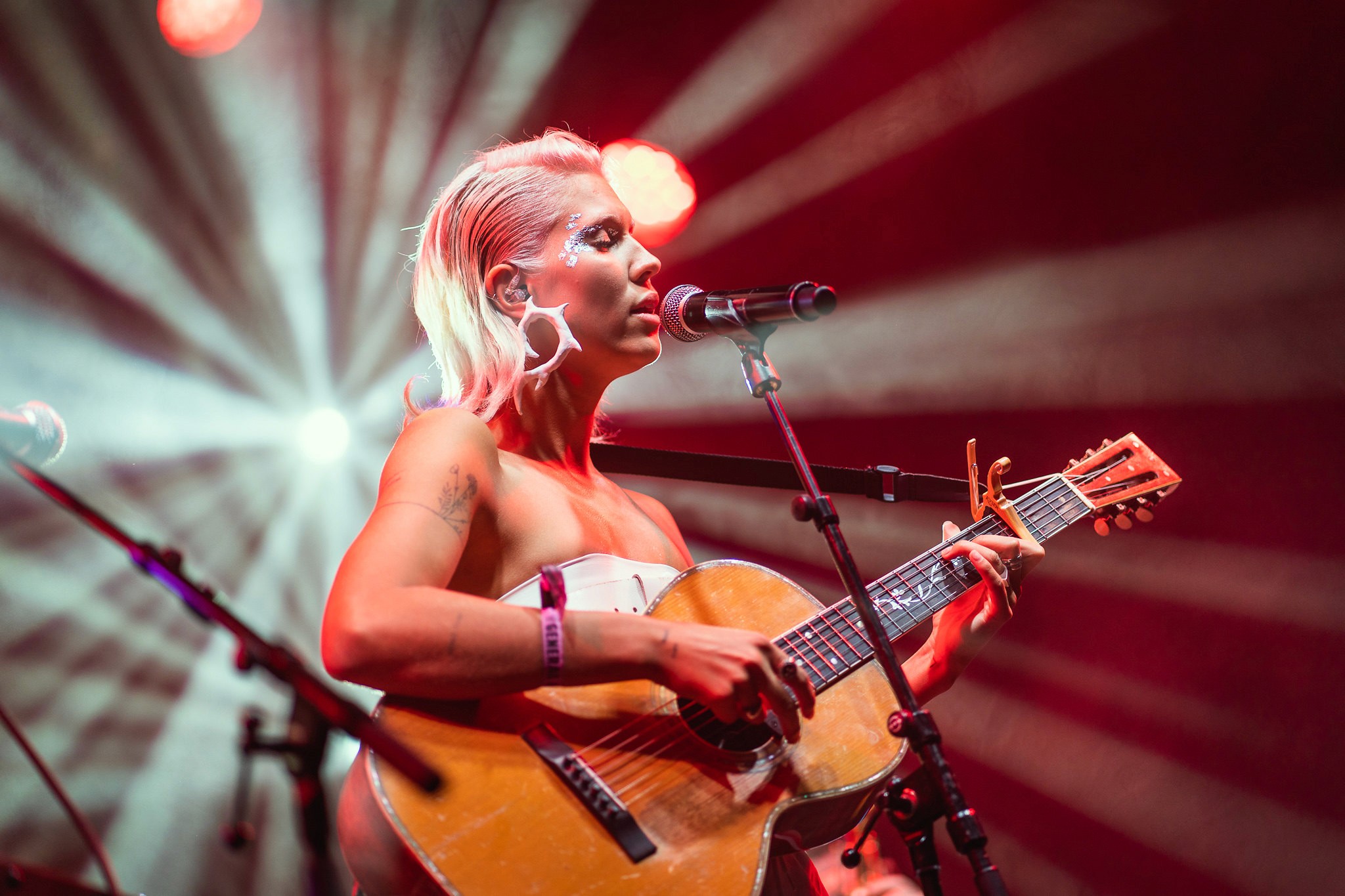 Musician Bríet performs on stage with an acoustic guitar during the Iceland Airwaves Festival, illuminated by dramatic red spotlights.