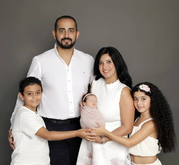 A family of five, including two older children, posing together while the parents hold their swaddled newborn.