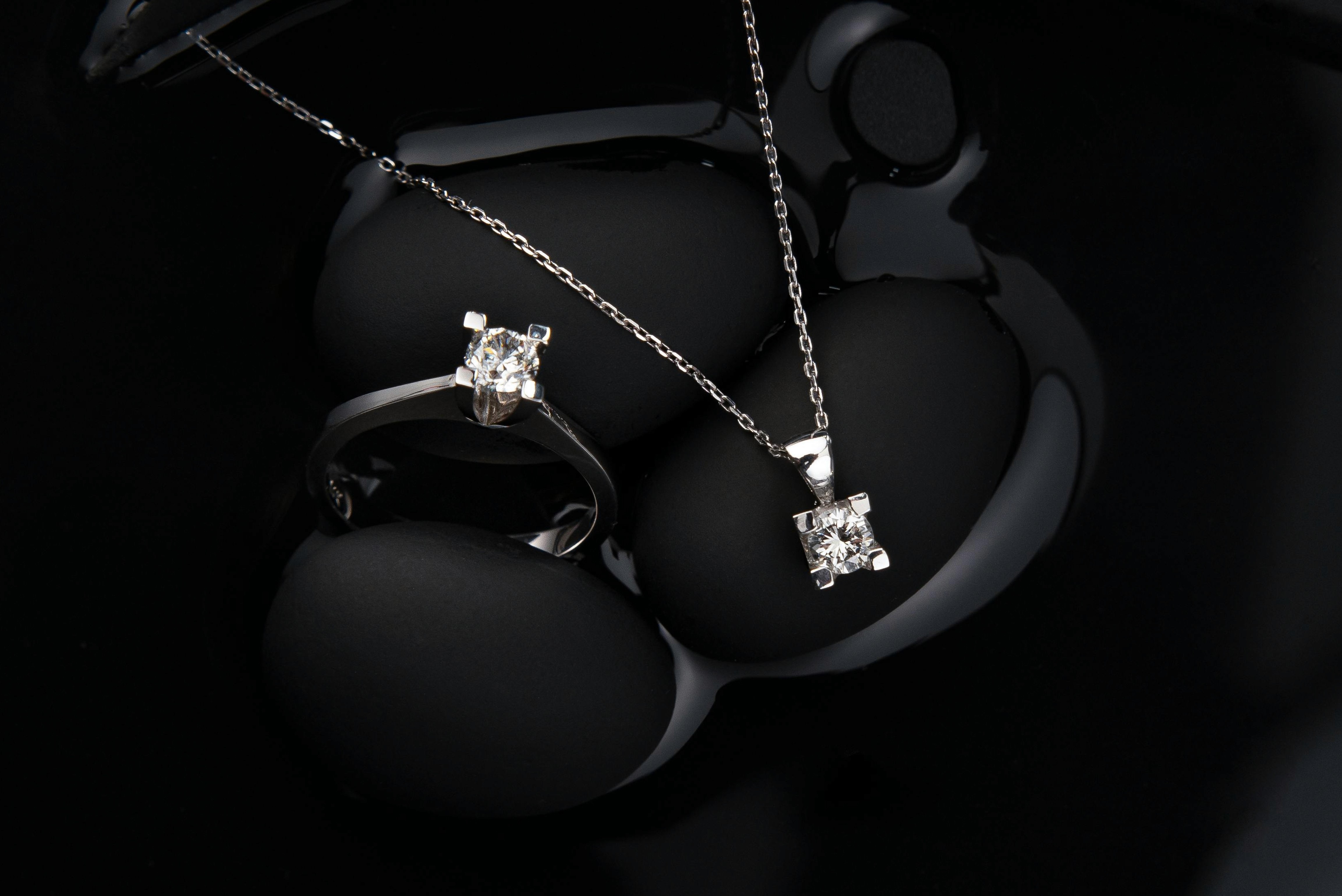 Close-up photo of a Nico Gems diamond ring and silver necklace on a black velvet surface.