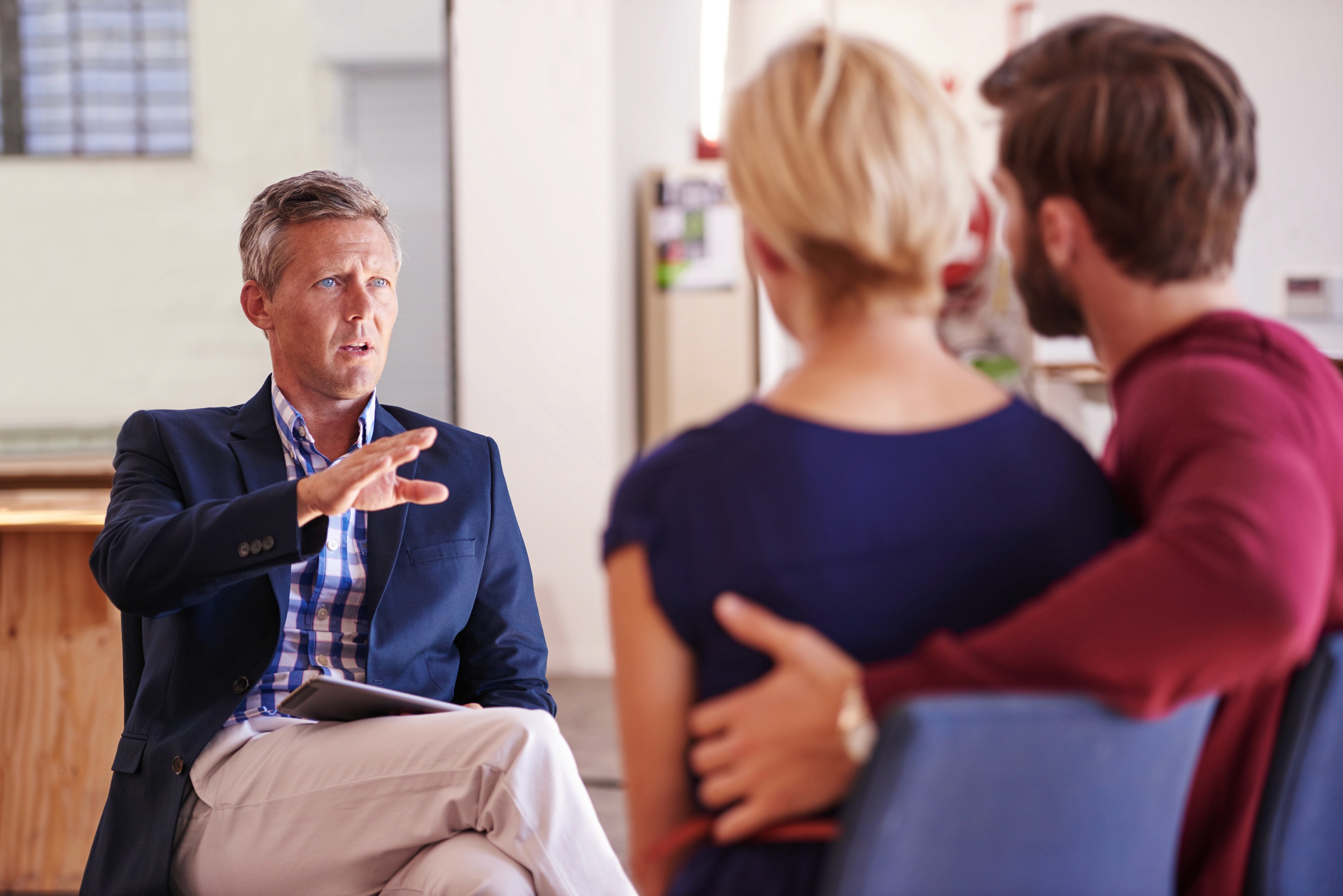 Man wearing headphones and a white t-shirt working on a laptop in soft natural light, with window shadows cast on the wall.
