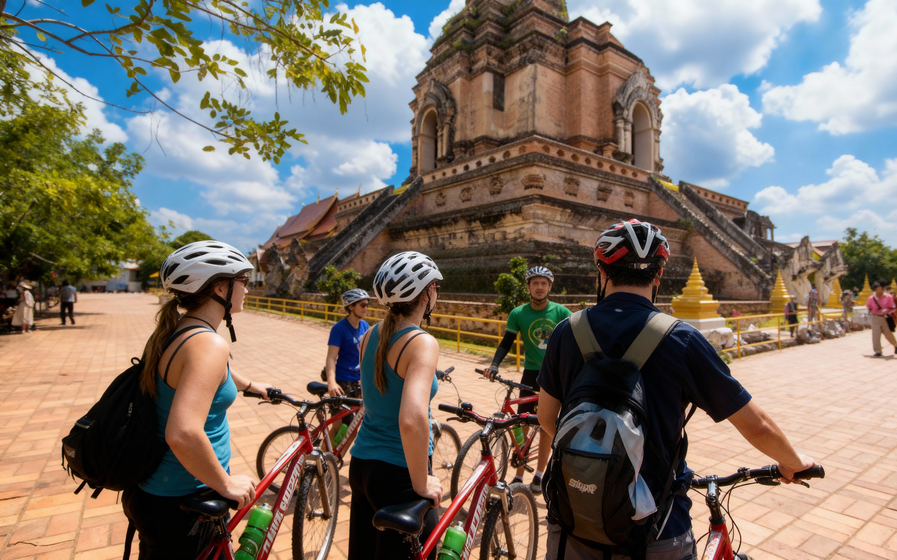 Group of cyclists wearing helmets pause with their bikes in front of Wat Chedi Luang, a historic brick temple in Chiang Mai’s Old City, on a sunny day with blue skies and scattered clouds.