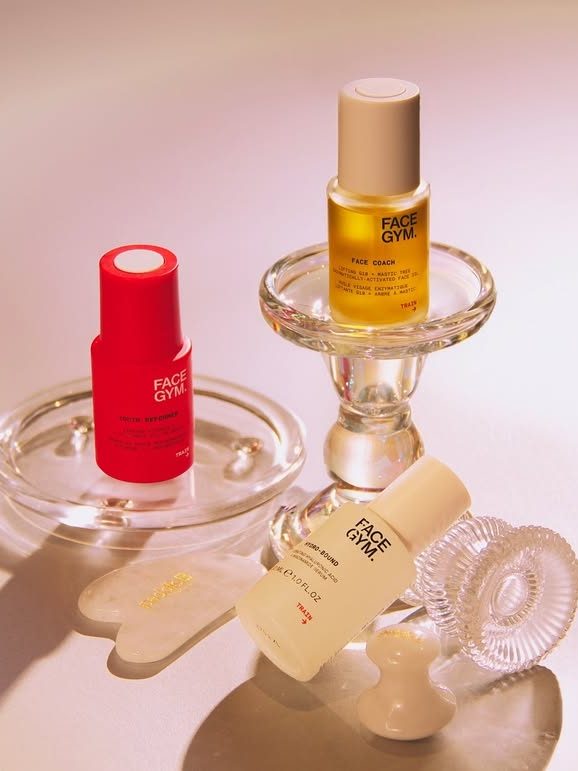 Three Face Gym skincare products on a glass display, featuring vibrant packaging and a jade roller.