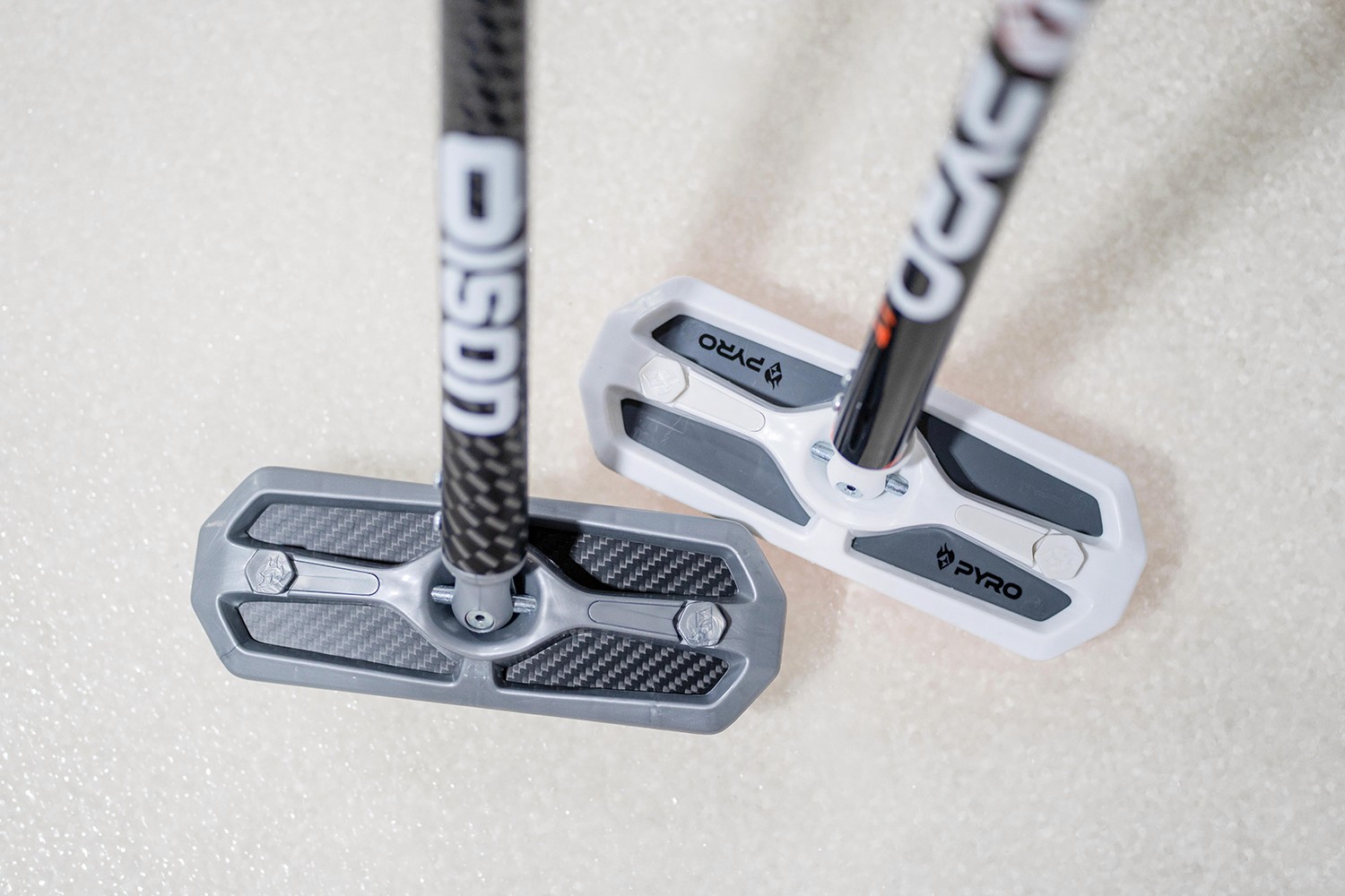 a silver and white colored curling broom beside eachother on a ice surface