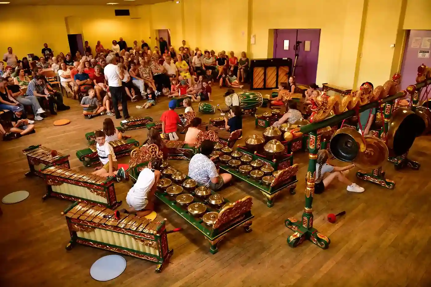 Un public regarde des enfants jouer du gamelan dans une salle de concert.