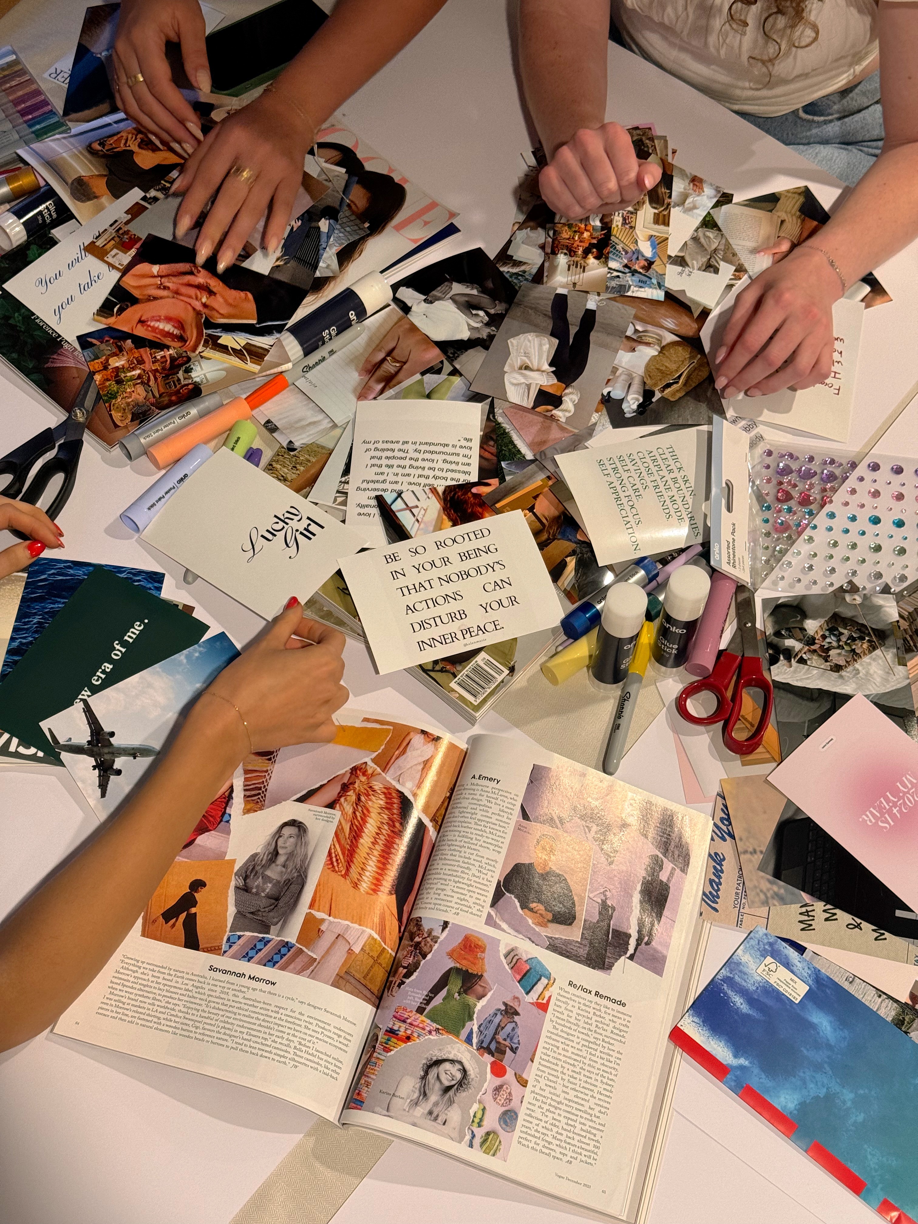 a flat lay with a bunch of hands reaching onto the table that is full of paint, paper, and magazines