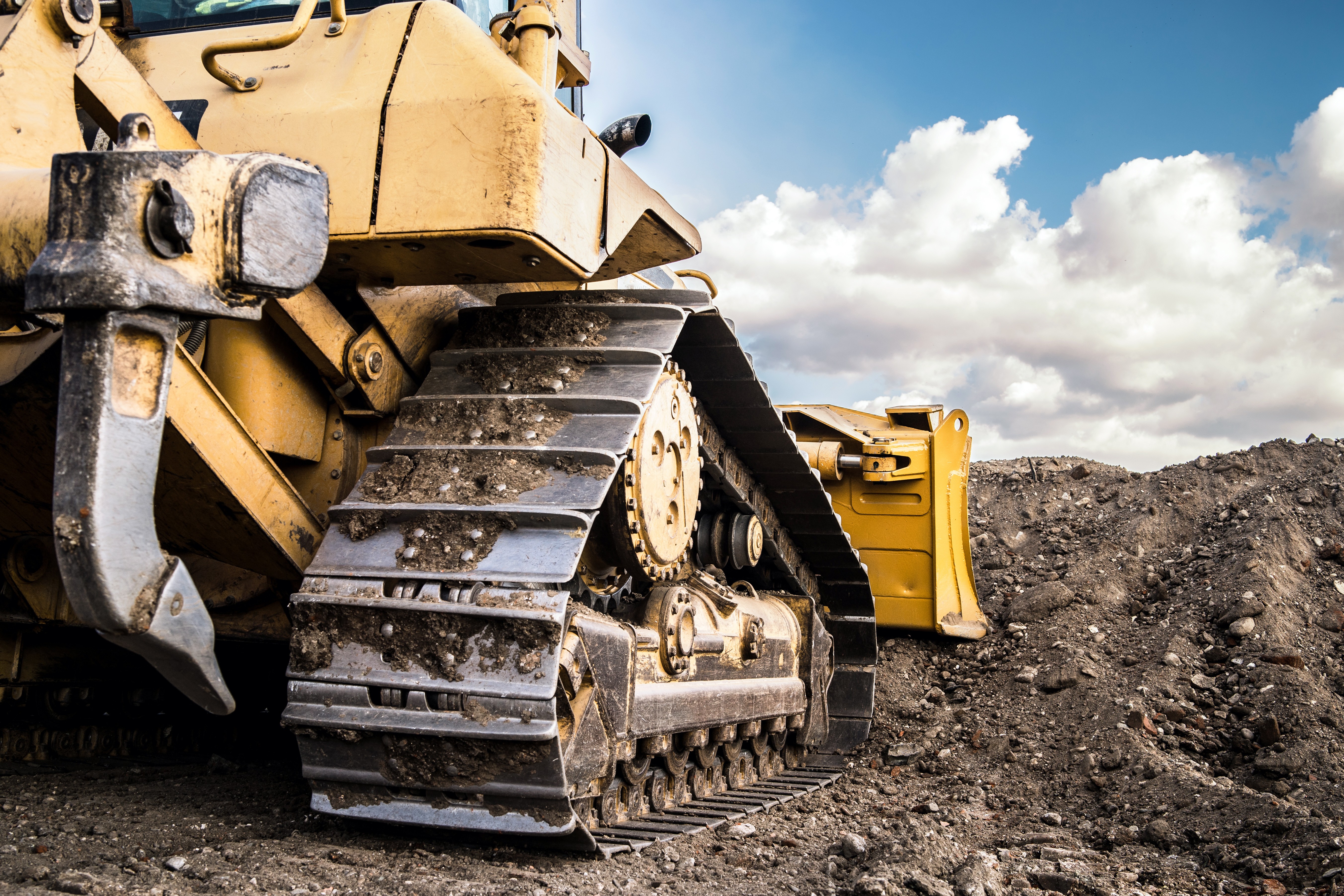 Close-up of a yellow bulldozer’s tracked wheels on rugged terrain at a mining site, showing details of earthmoving equipment.