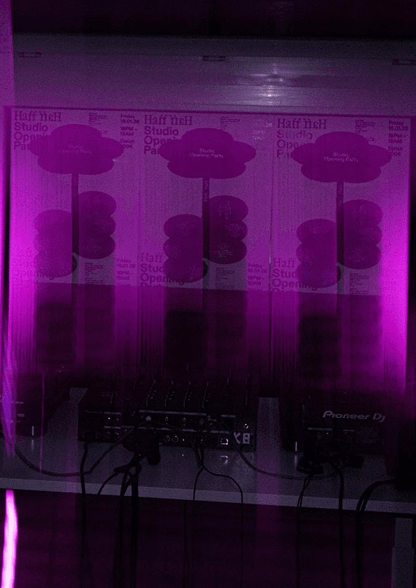 An experimental, long-exposure photograph of the DJ booth at the studio housewarming, featuring glowing pink neon light tubes and motion-blurred "Studio Opening Party" posters in the background. This artistic shot emphasizes the studio’s expertise in immersive event branding and dynamic visual storytelling.