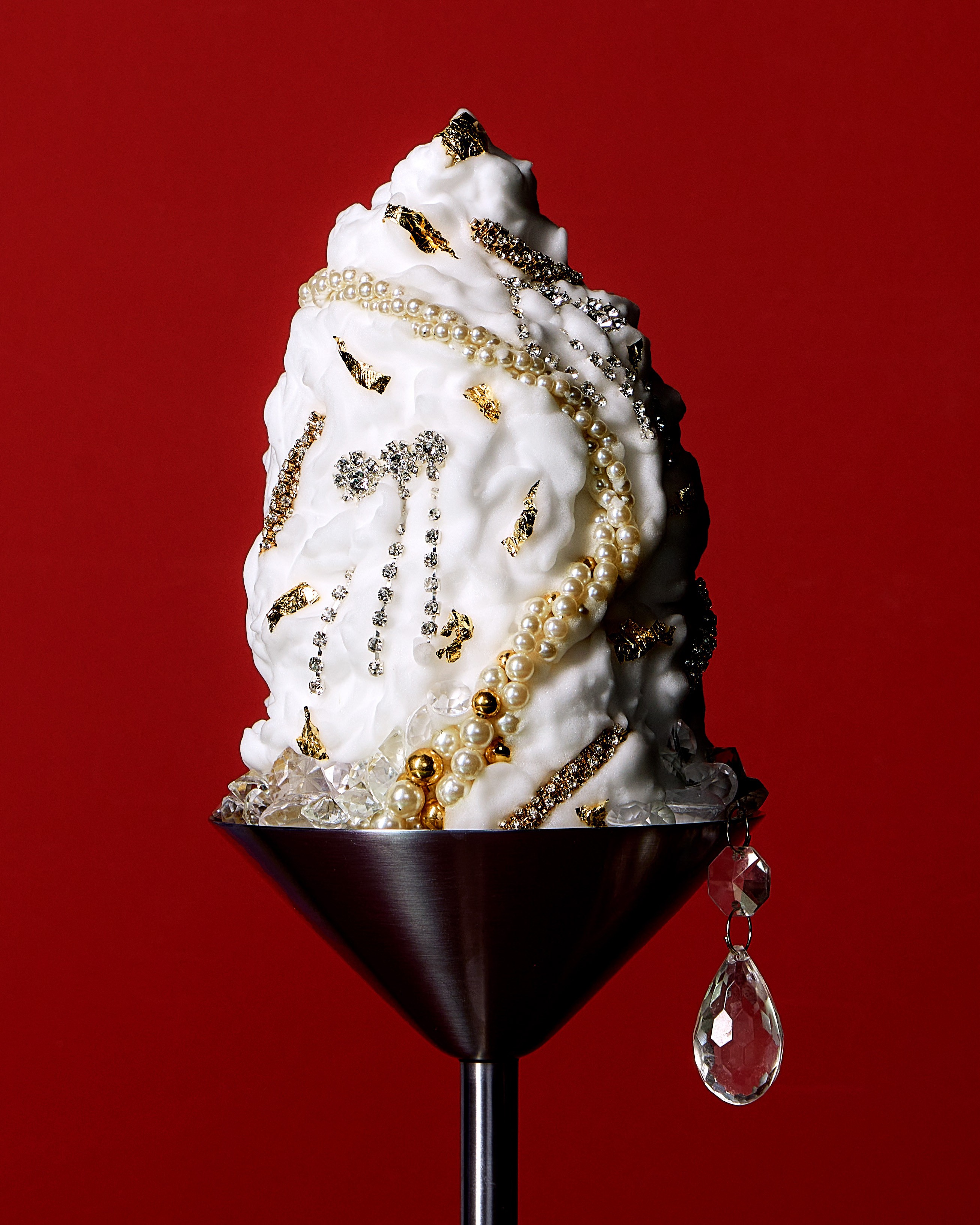 Jeweled white dessert with pearls and gold leaf against a red background