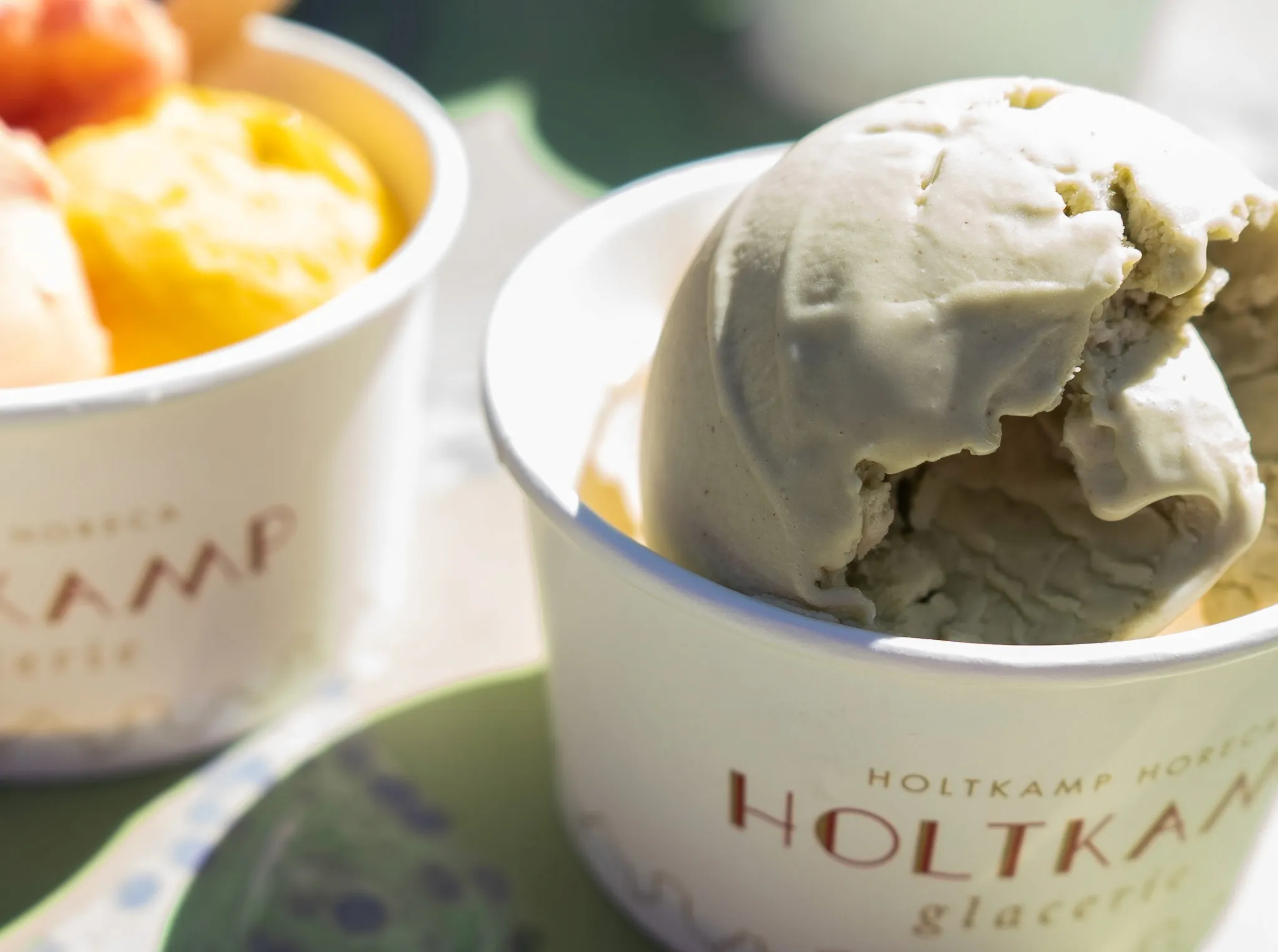 Two bowls of gelato: one with green tea flavor and another with assorted fruit flavors, on a sunny table.