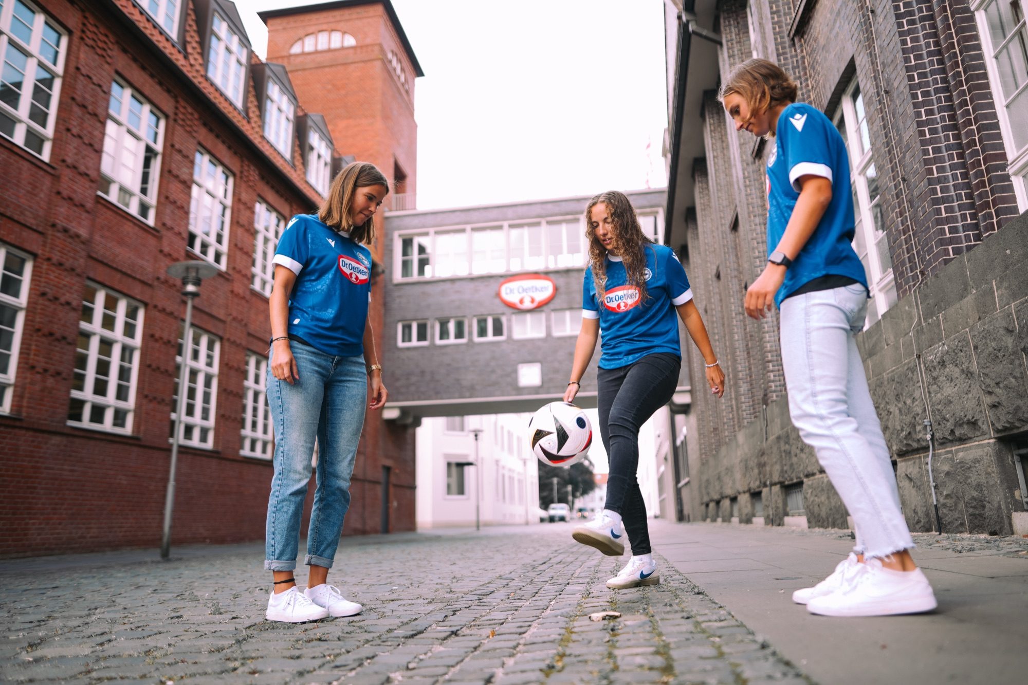 Spielerinnen im blauen Trikot spielen sich in einer Straße den Ball zu