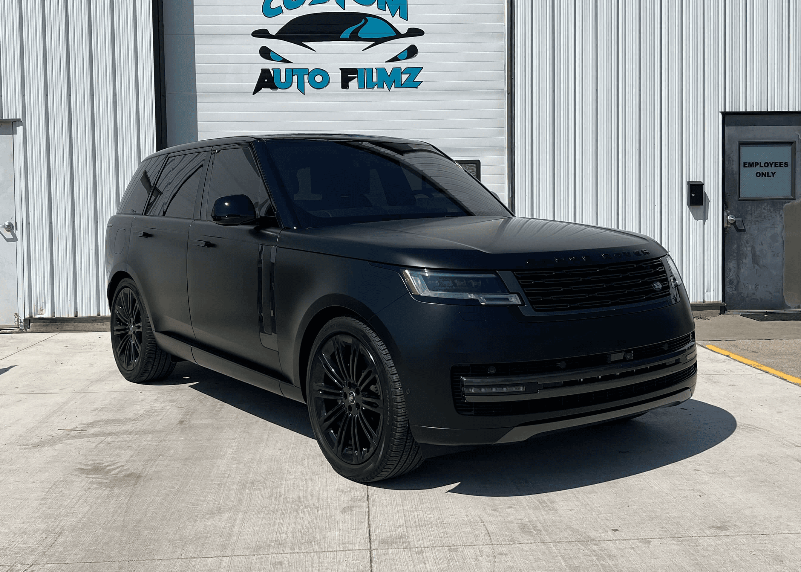 A matte black Range Rover is parked on a concrete driveway in front of a white industrial building.