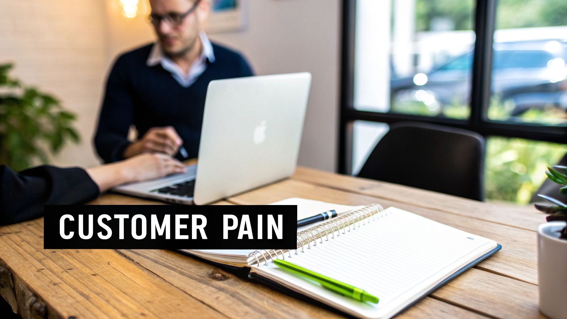 Two individuals collaborating at a wooden table with a laptop and notebook, addressing customer pain points.