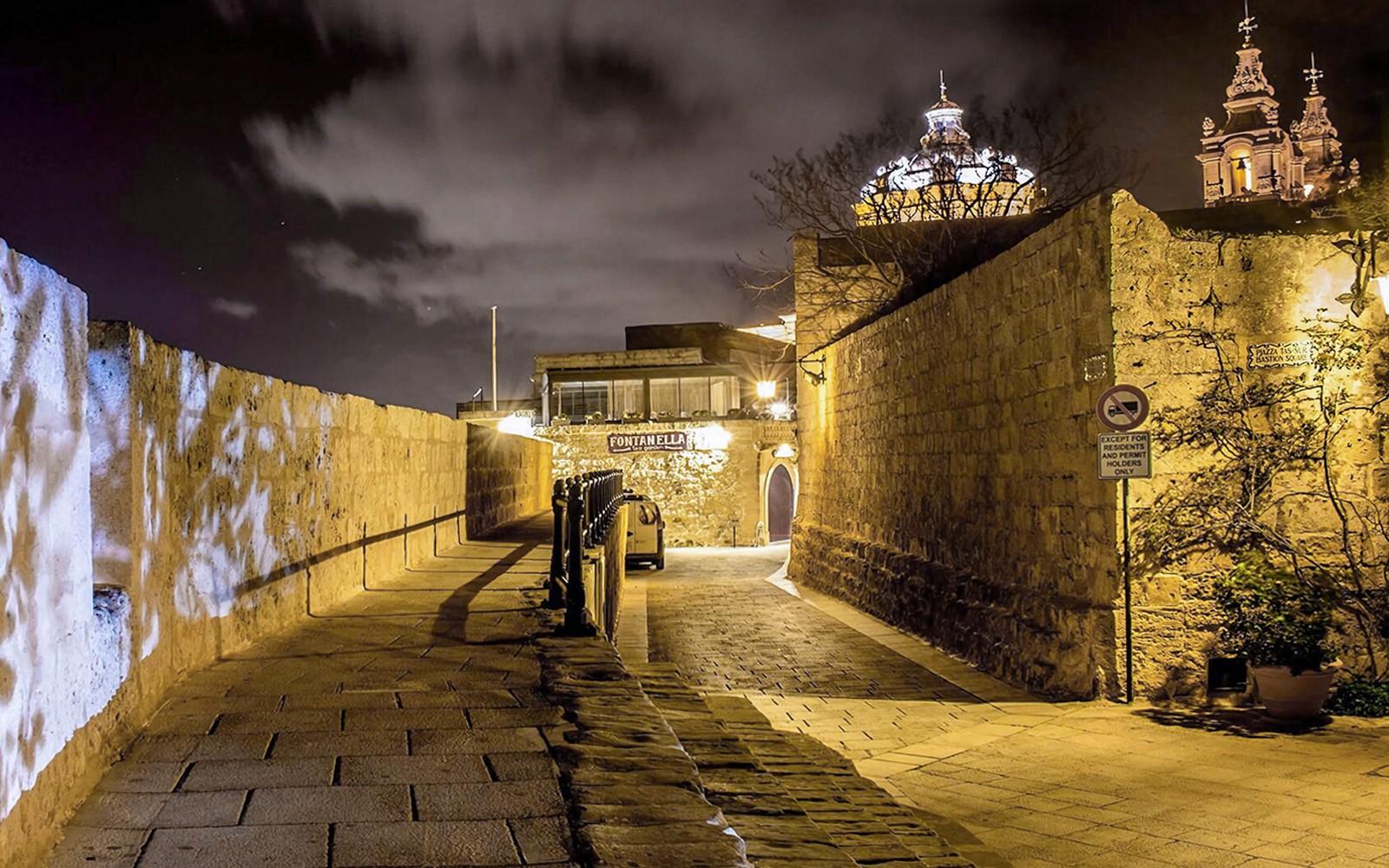 Historic stone pathway in Malta illuminated at night with church domes in the background.