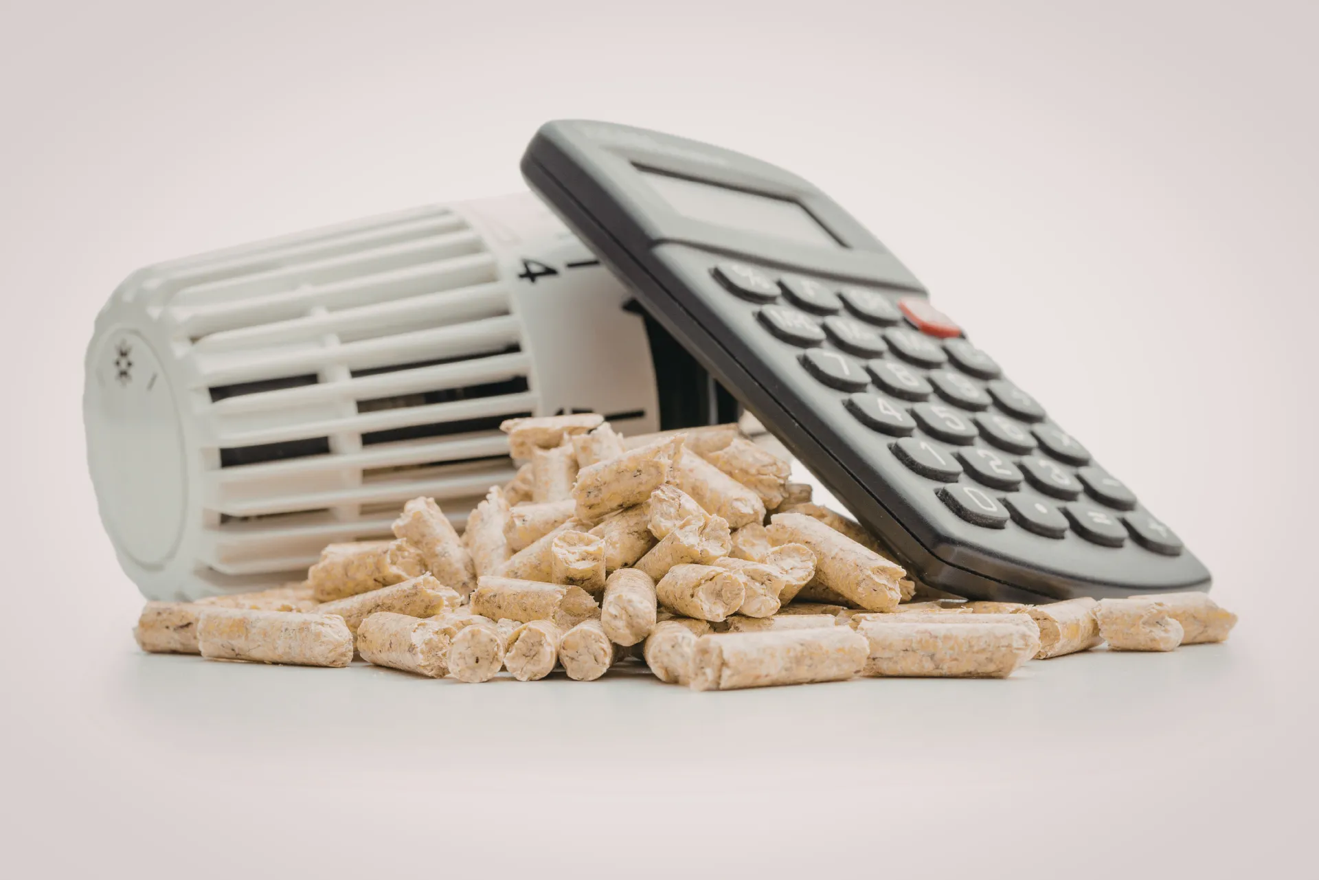 Ein Heizungsregler, ein Taschenrechner und Pelletholz auf einem Haufen aufeinandern angelehnt.